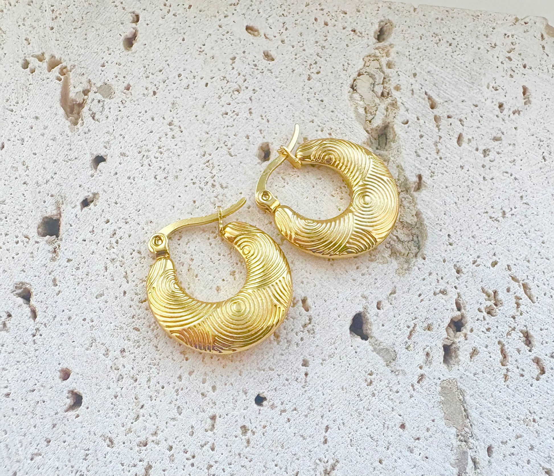 Gold hoop earrings on a textured stone surface