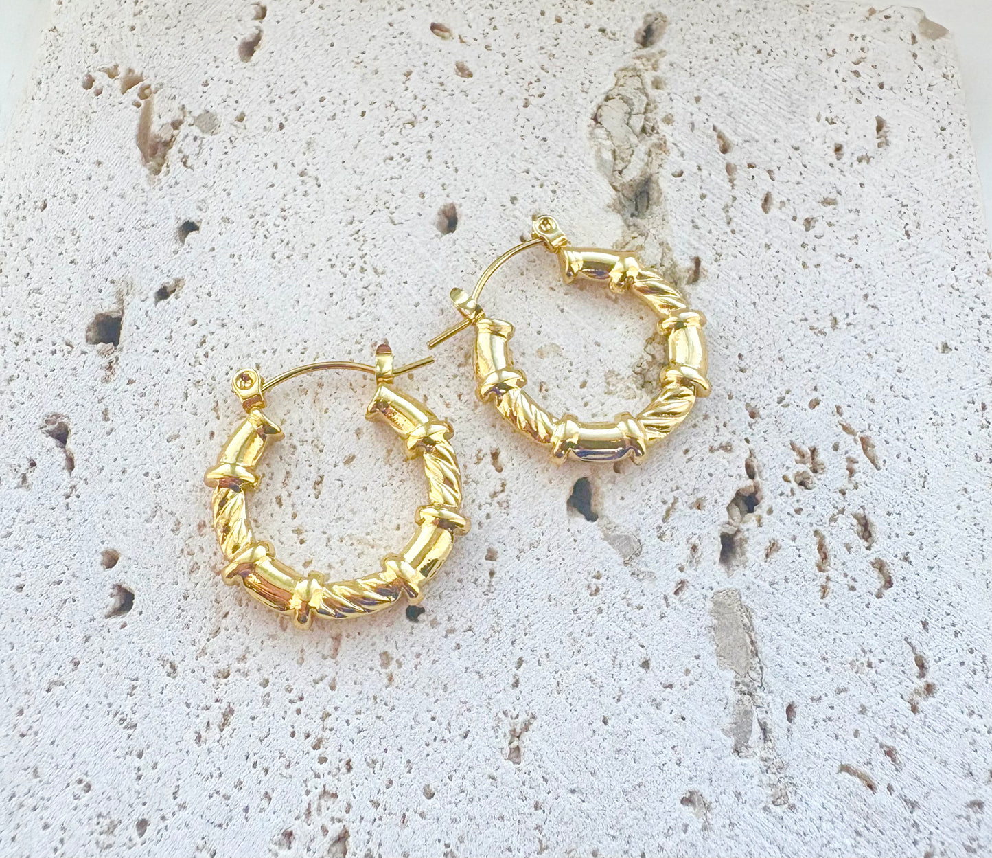 Gold hoop earrings on a textured stone surface