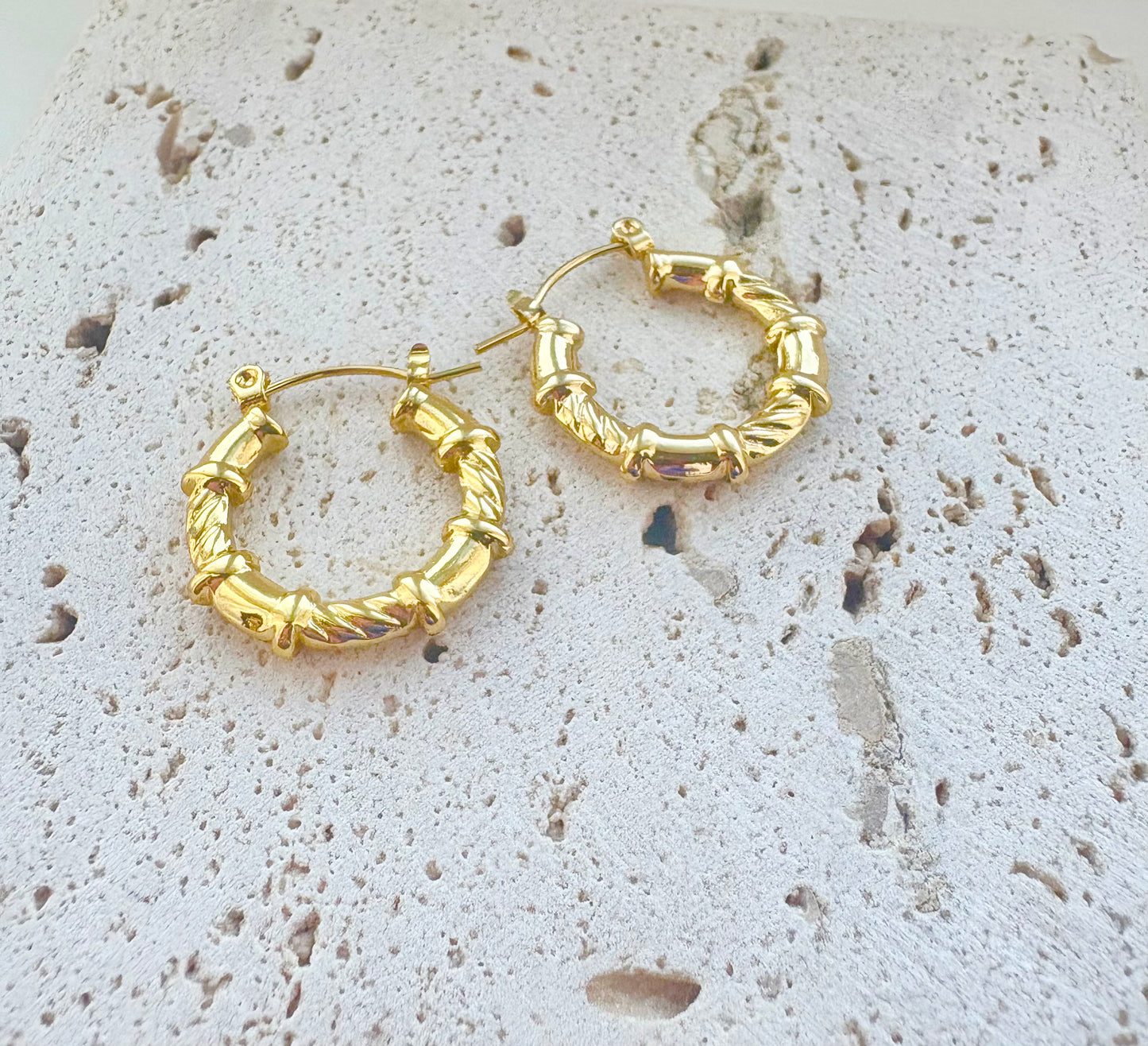 Gold hoop earrings on a textured stone surface