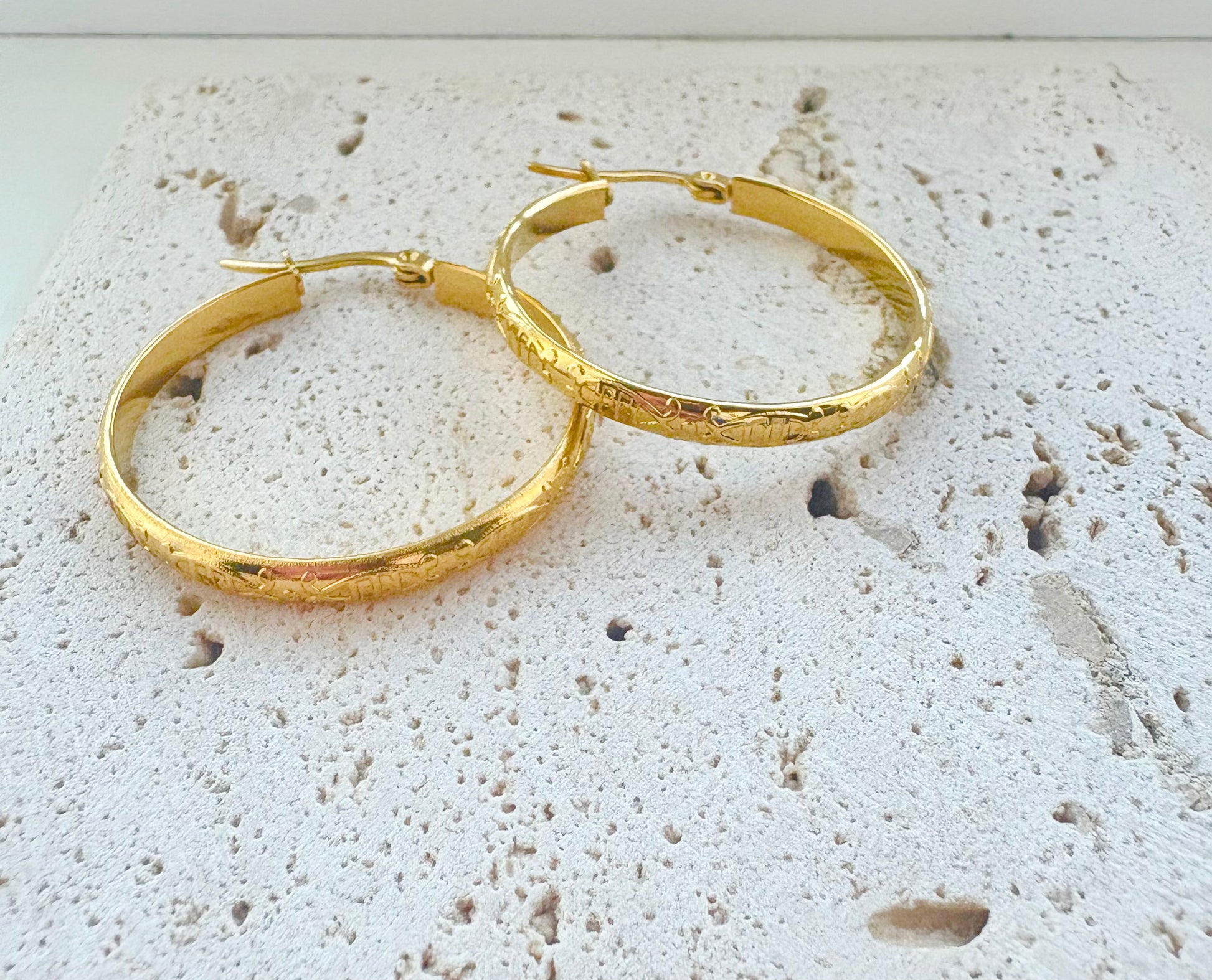 Gold hoop earrings on a textured white surface