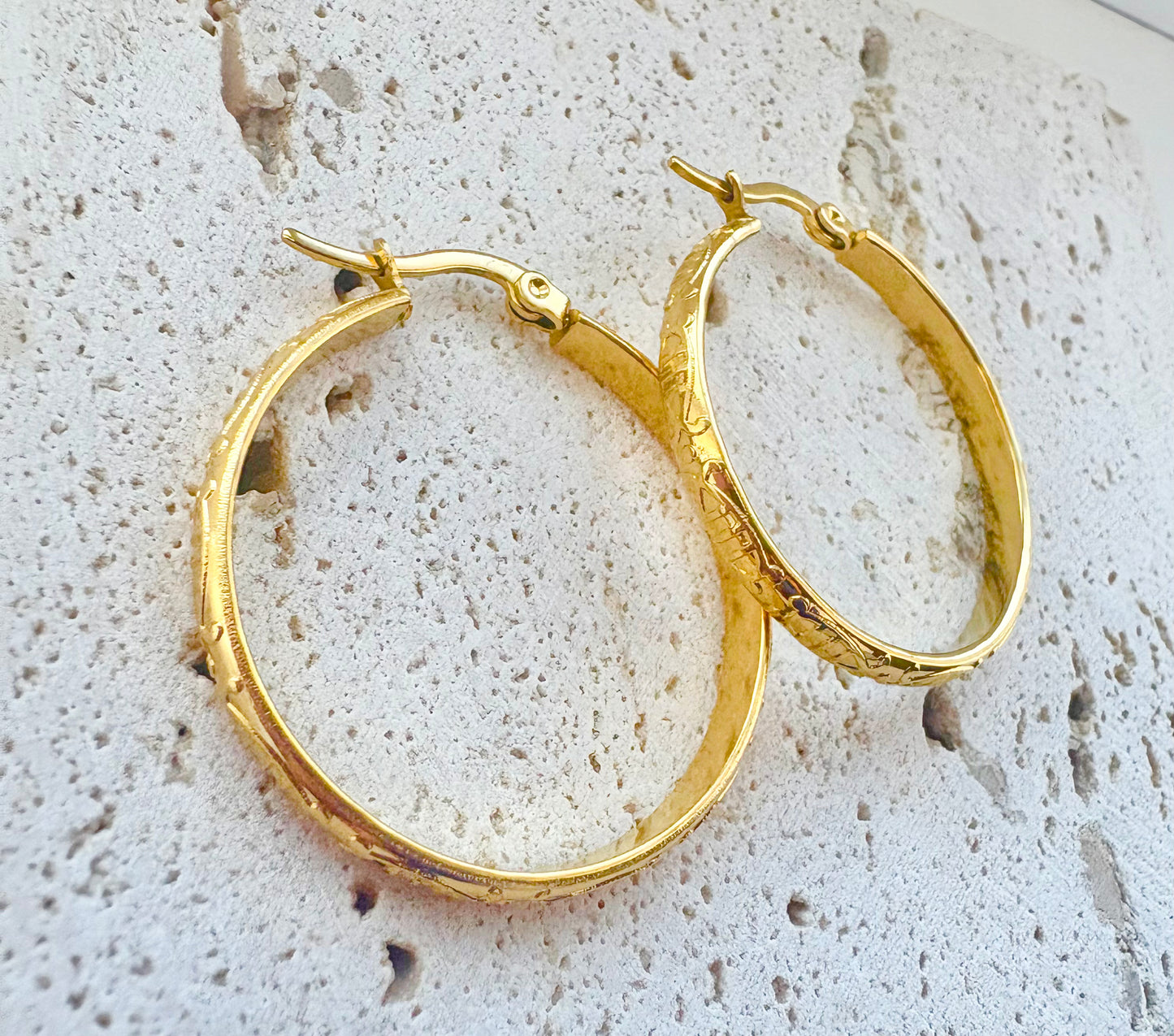 Gold hoop earrings on a textured stone surface