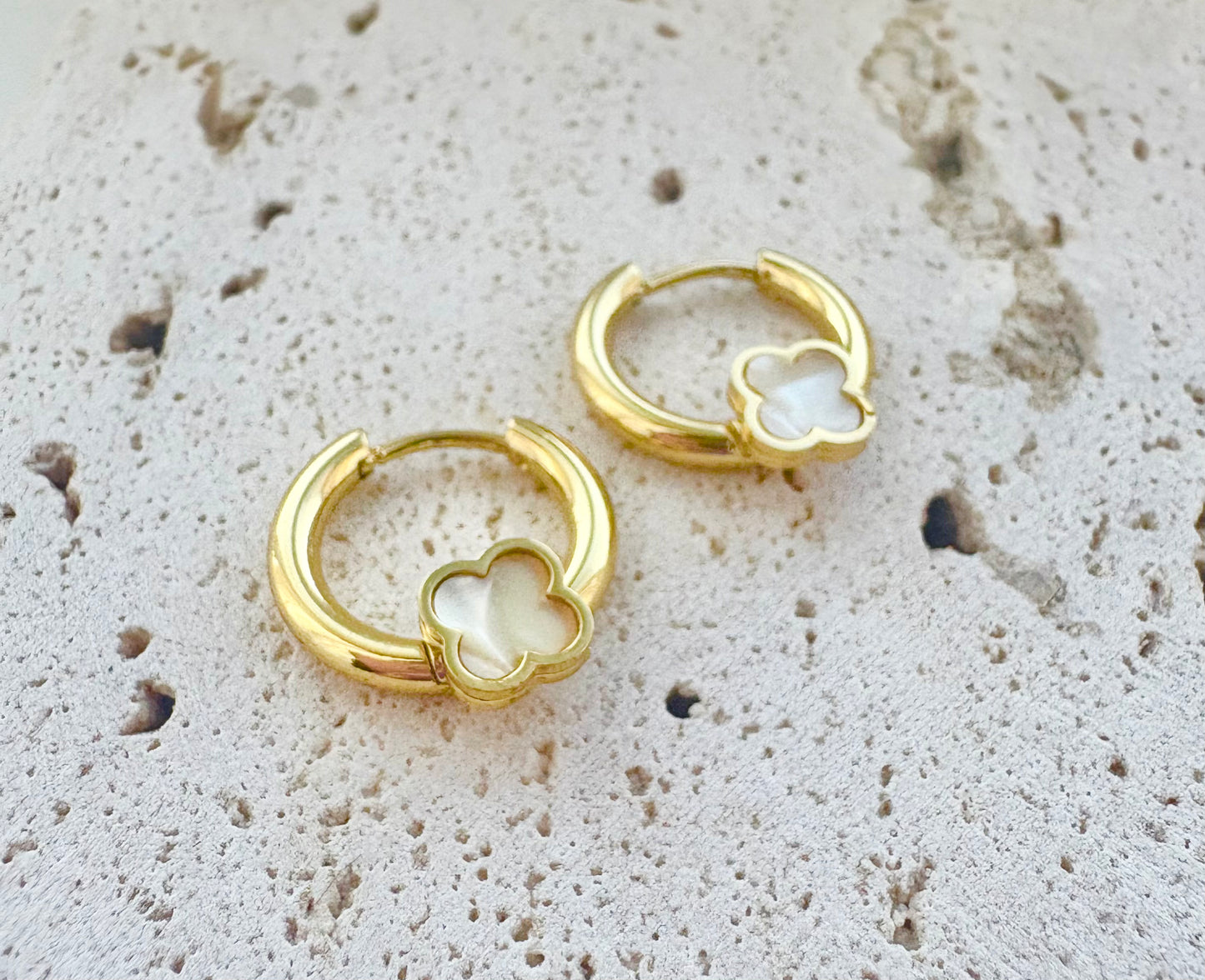 Gold hoop earrings with clover-shaped designs on a textured beige surface