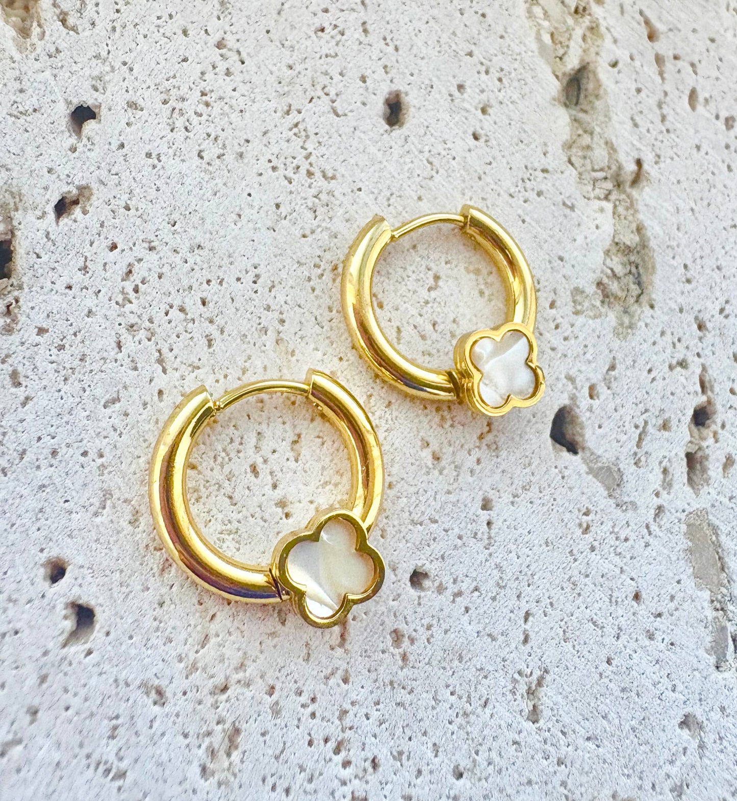Gold hoop earrings with clover designs on a textured stone surface