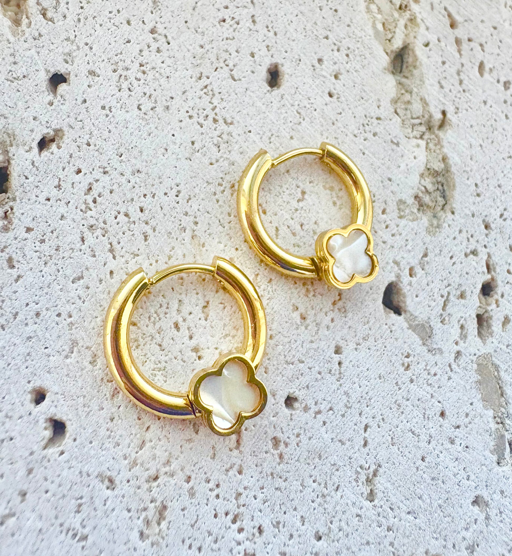 Gold hoop earrings with clover designs on a textured stone surface