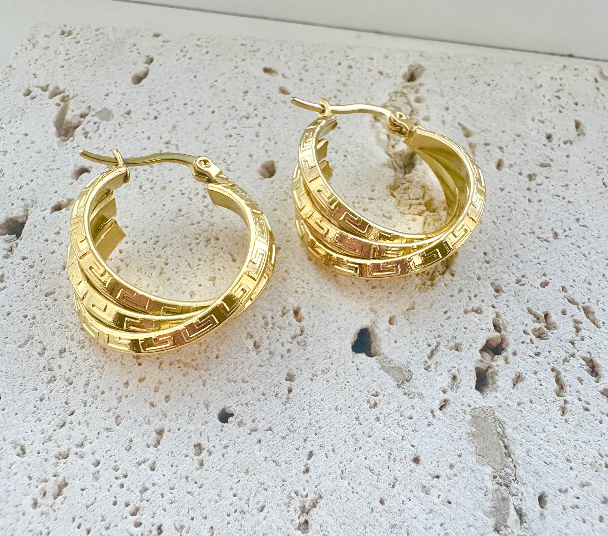Gold hoop earrings on a textured stone surface