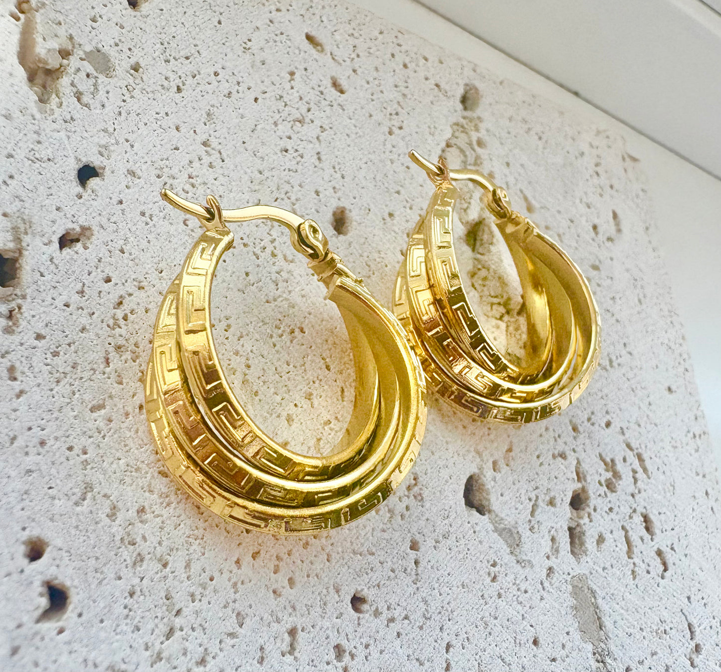 Gold hoop earrings on a textured stone surface
