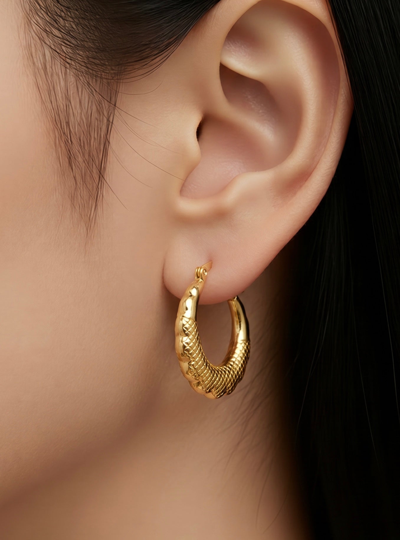 Gold hoop earring worn by a person with dark hair.