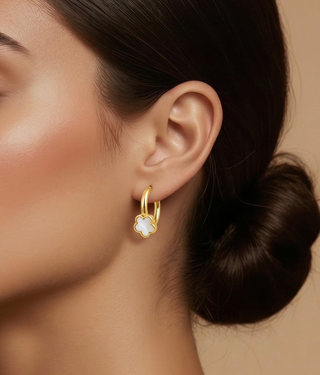 Gold hoop earring with a clear gemstone worn by a person with dark hair.