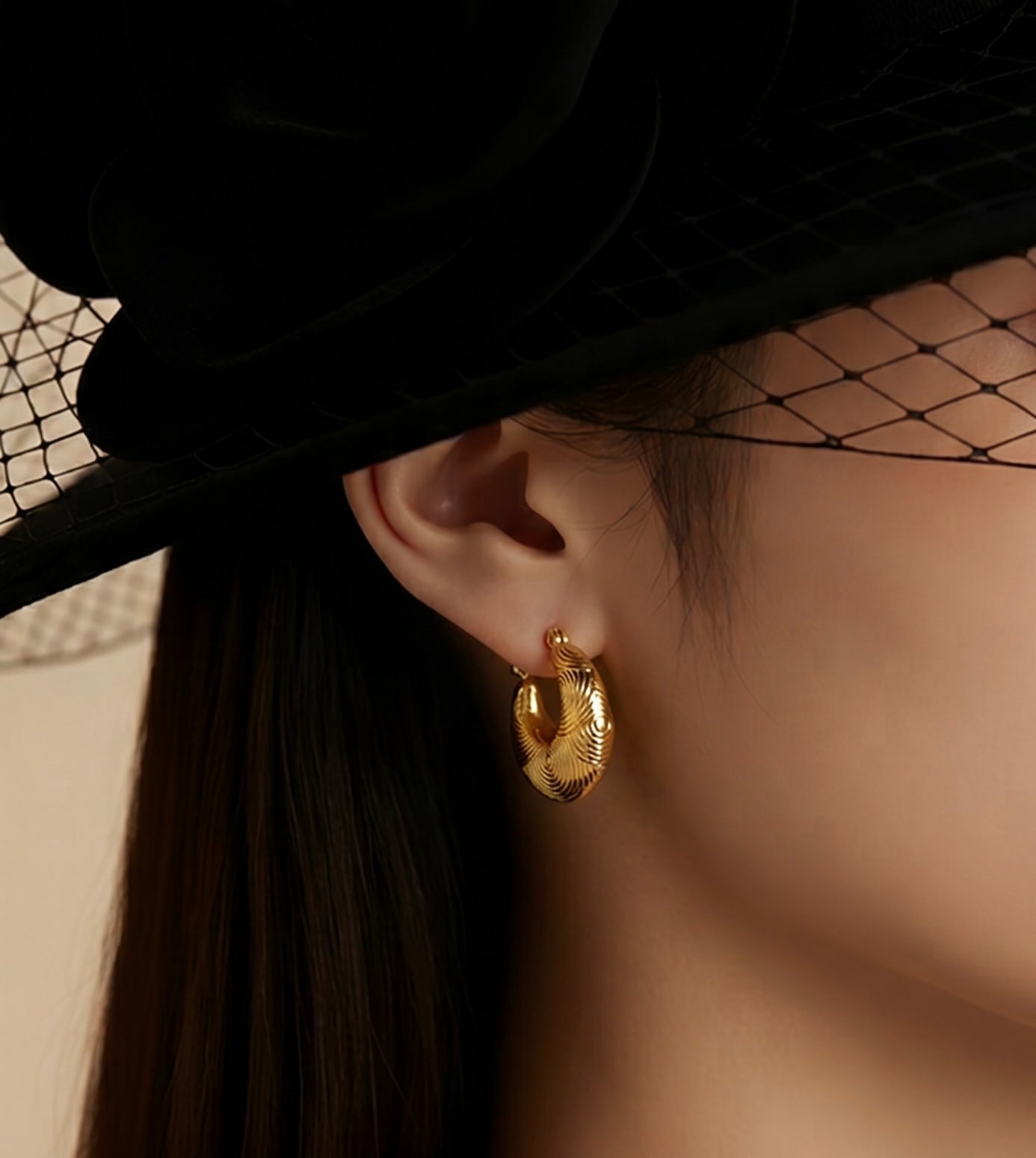 Gold hoop earrings worn by a person with a black hat and veil.