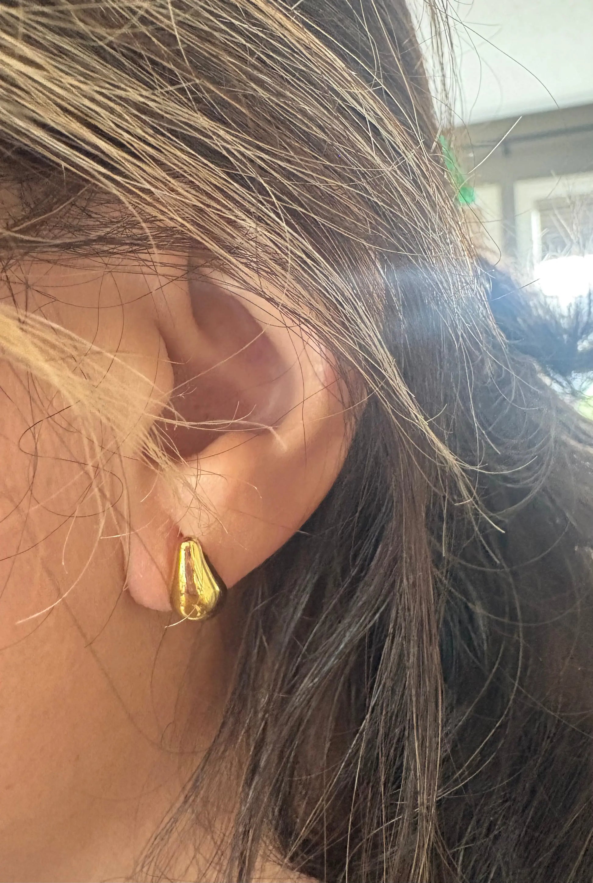 Close-up of a person wearing a gold hoop earring with blurred background