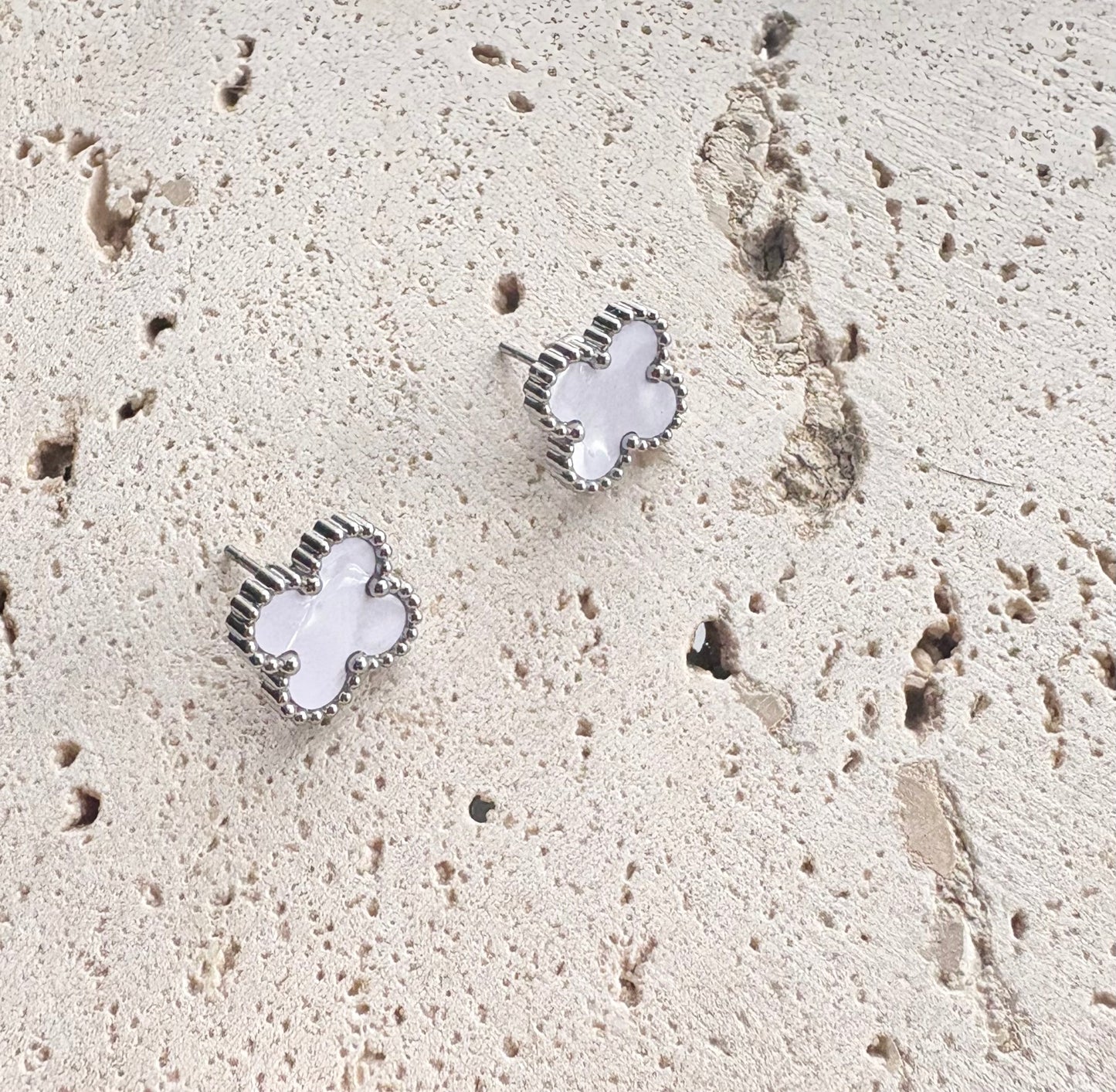 Clover-shaped earrings on a textured beige surface