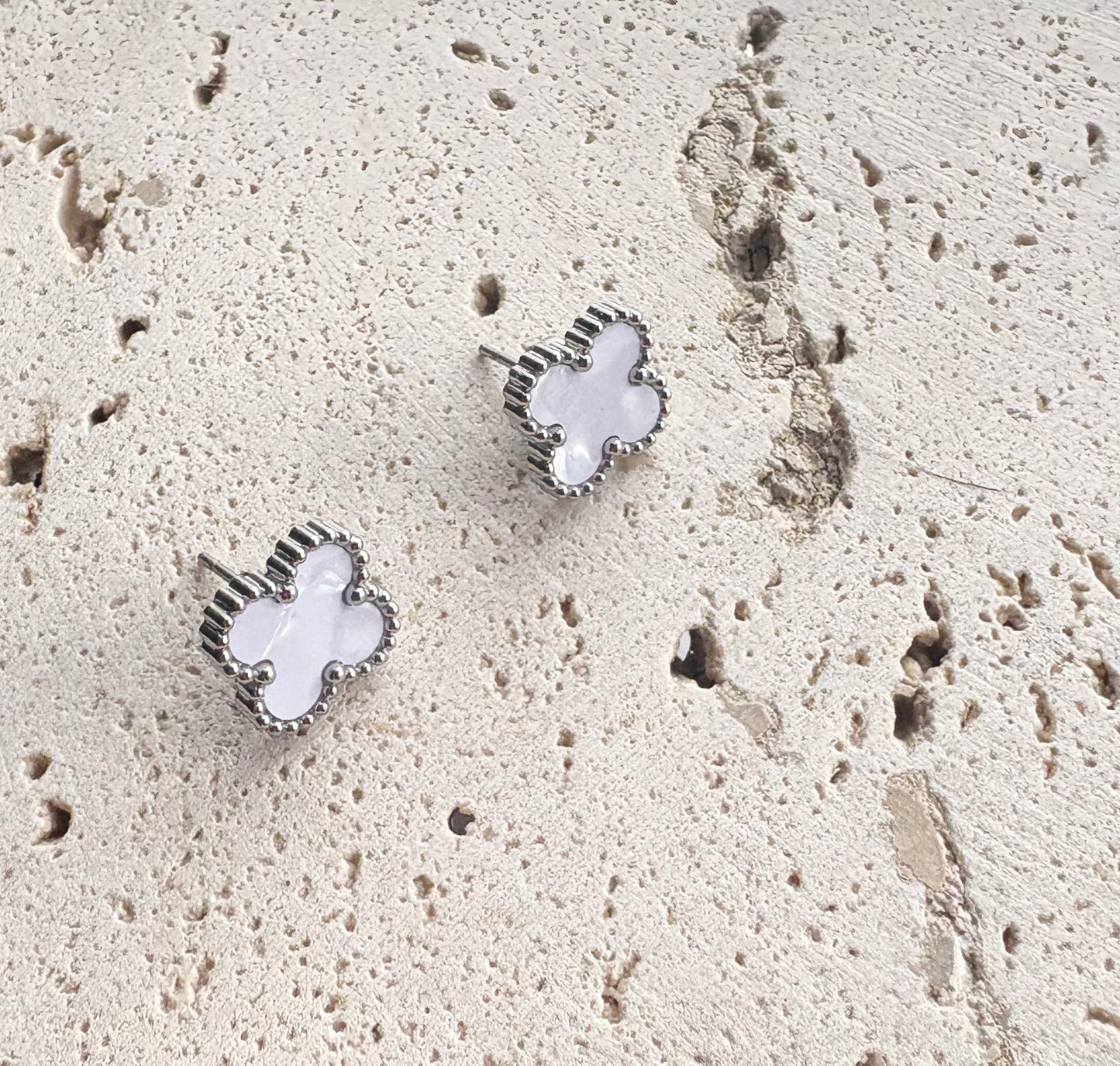  Silver Clover earrings with a white stone on a textured beige surface