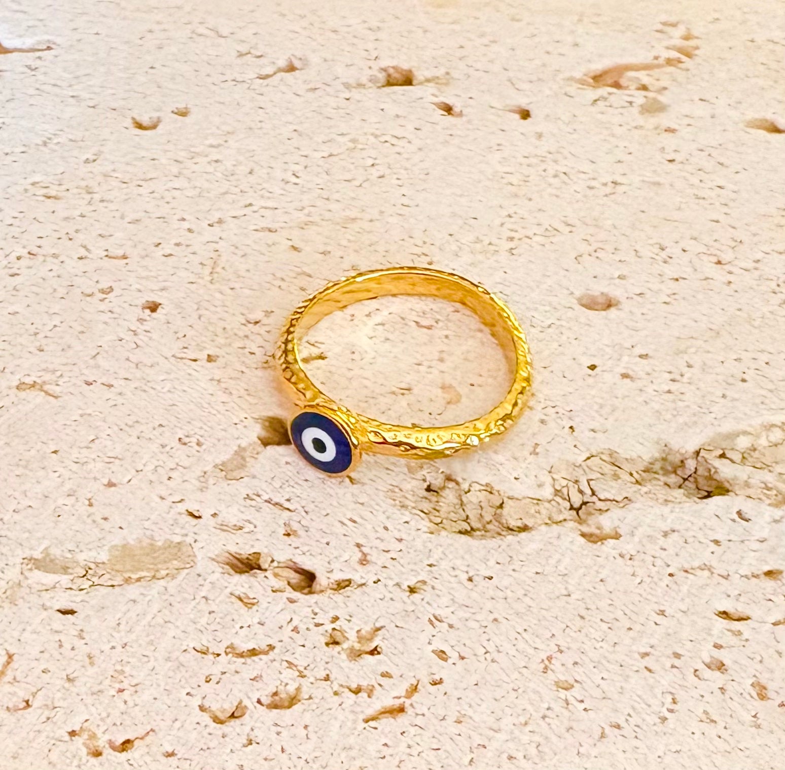 A textured gold ring with a small blue and white evil eye charm