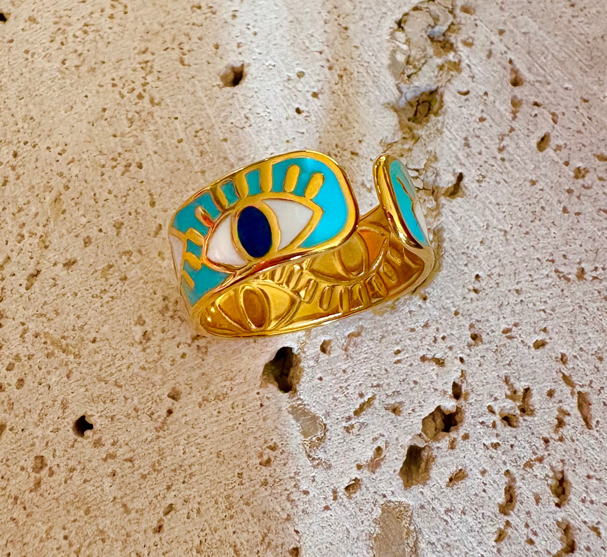 A gold-plated cuff ring featuring a turquoise, white, and dark blue evil eye design.