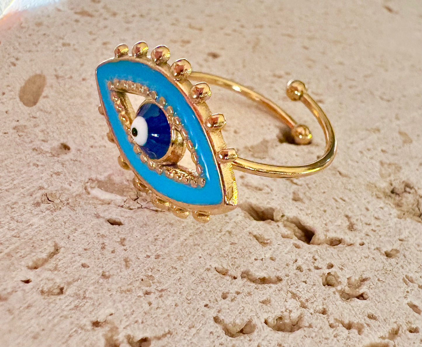A gold-plated open ring featuring a large blue enamel evil eye design with a central white and black bead
