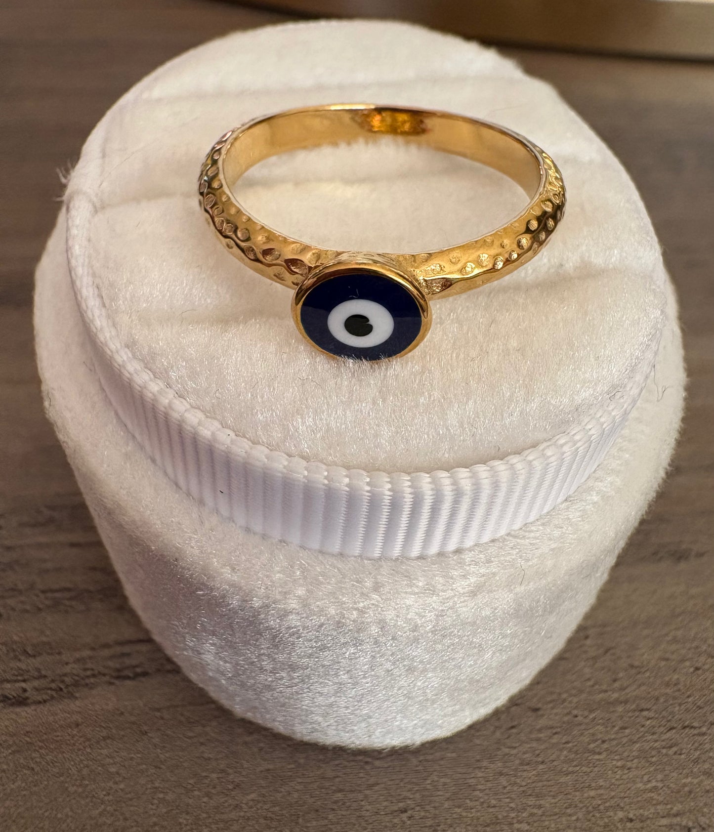A gold band ring with a textured pattern and a central circular evil eye charm