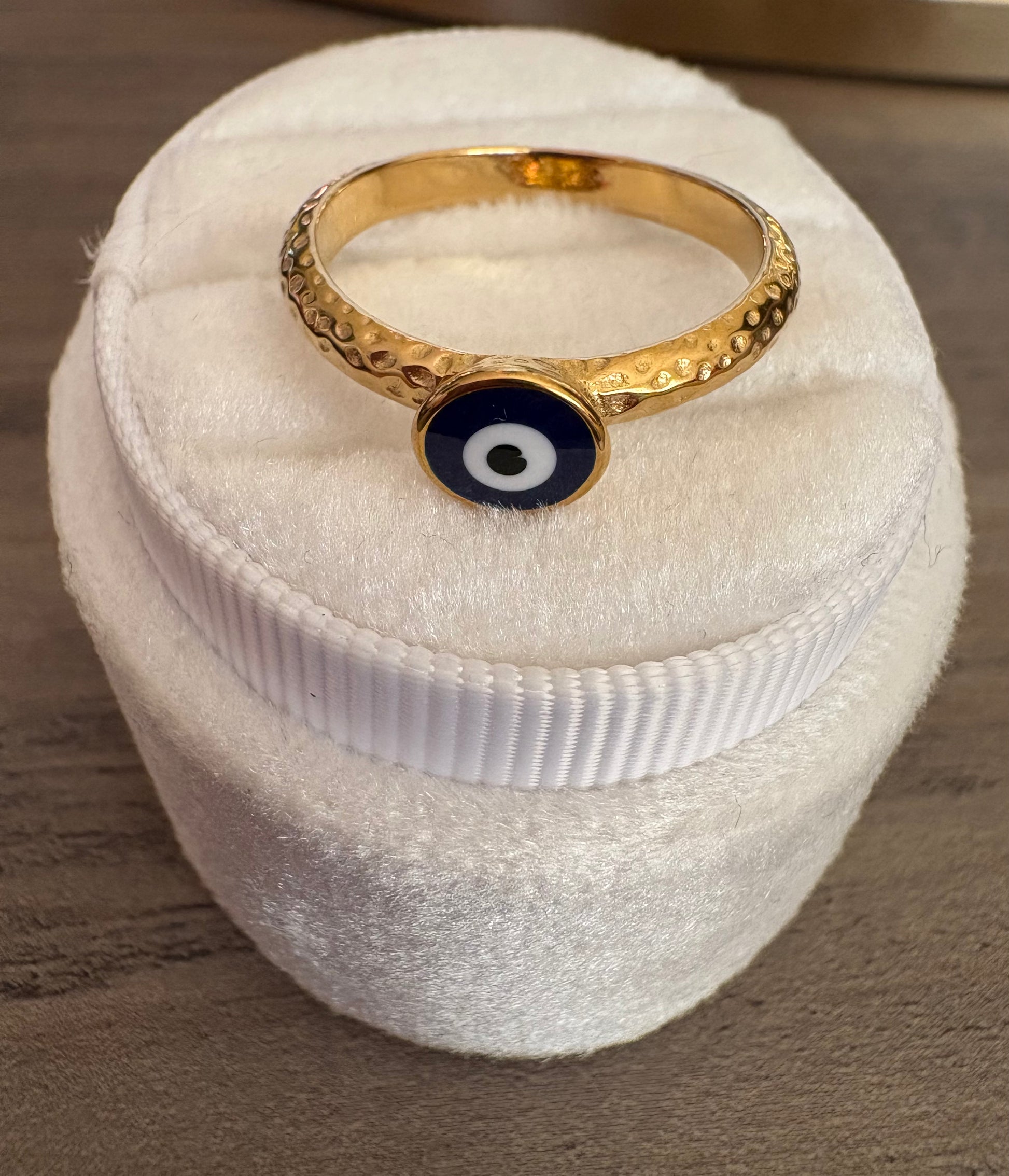 A gold band ring with a textured pattern and a central circular evil eye charm