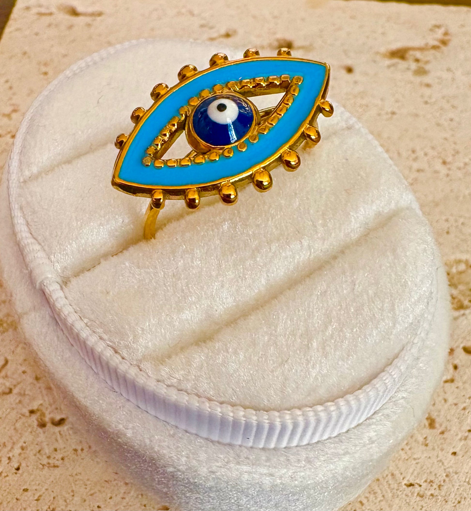 Gold and blue evil eye ring displayed on a white velvet jewelry box