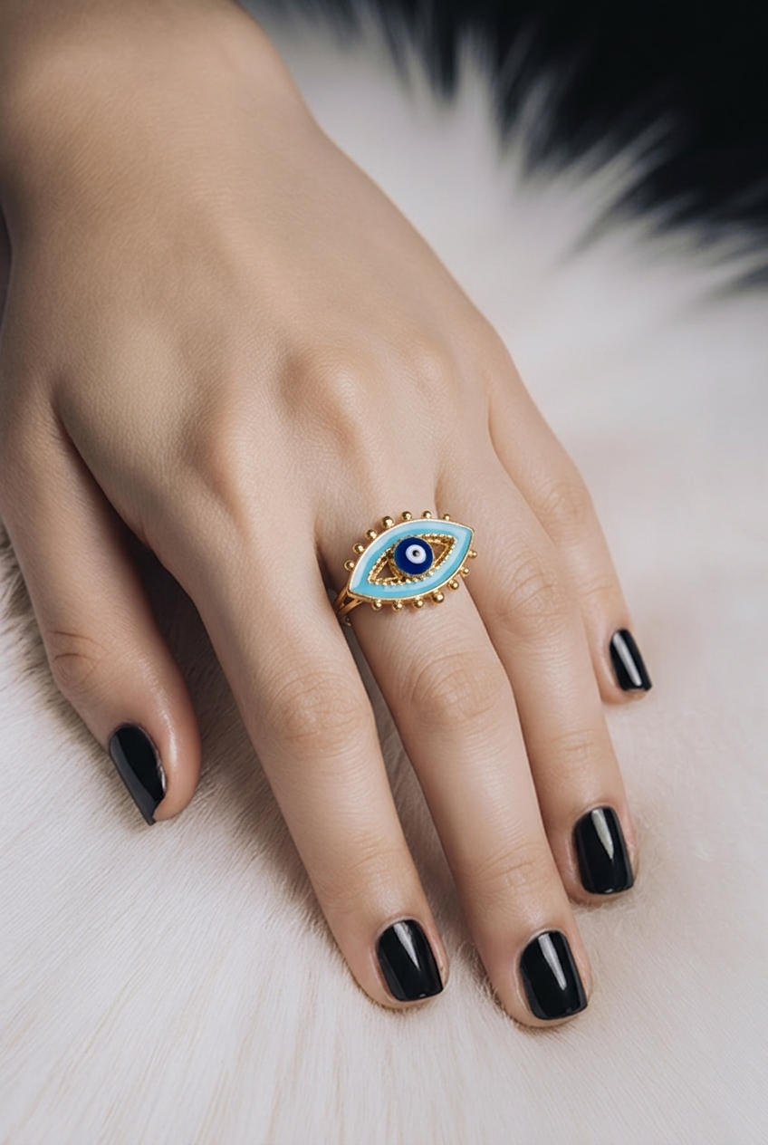 A gold ring with a turquoise and white evil eye design, worn on a hand 