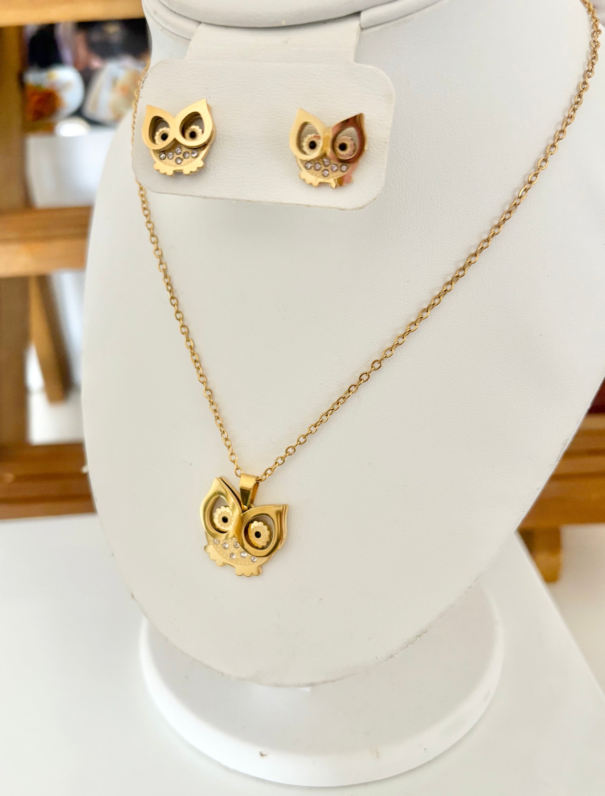 Gold owl pendant necklace and matching stud earrings displayed on a white jewelry bust. 