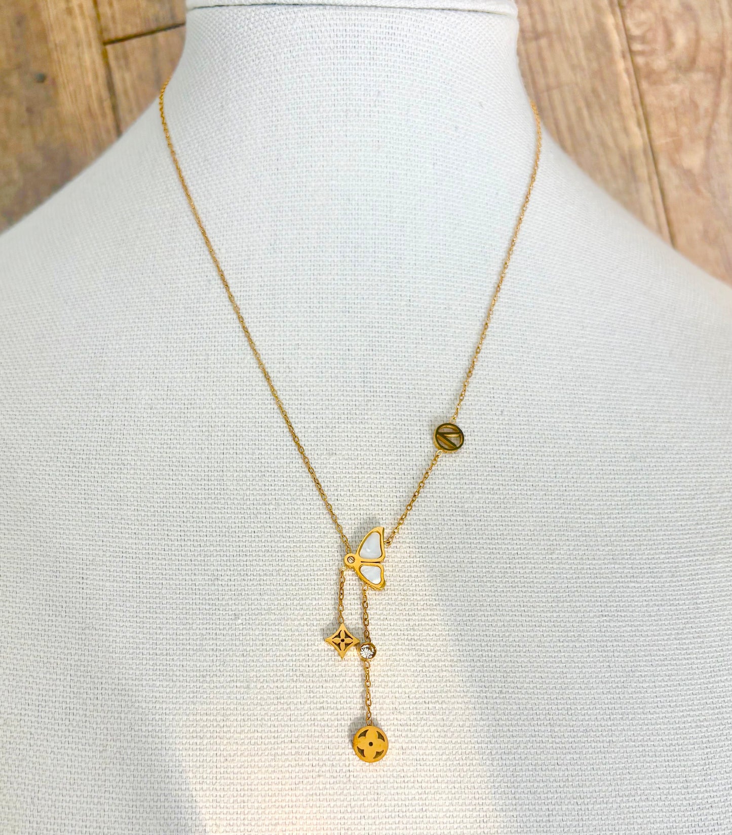 A delicate gold Y-necklace a central butterfly charm with dangling clover and flower motifs, alongside a small round charm.