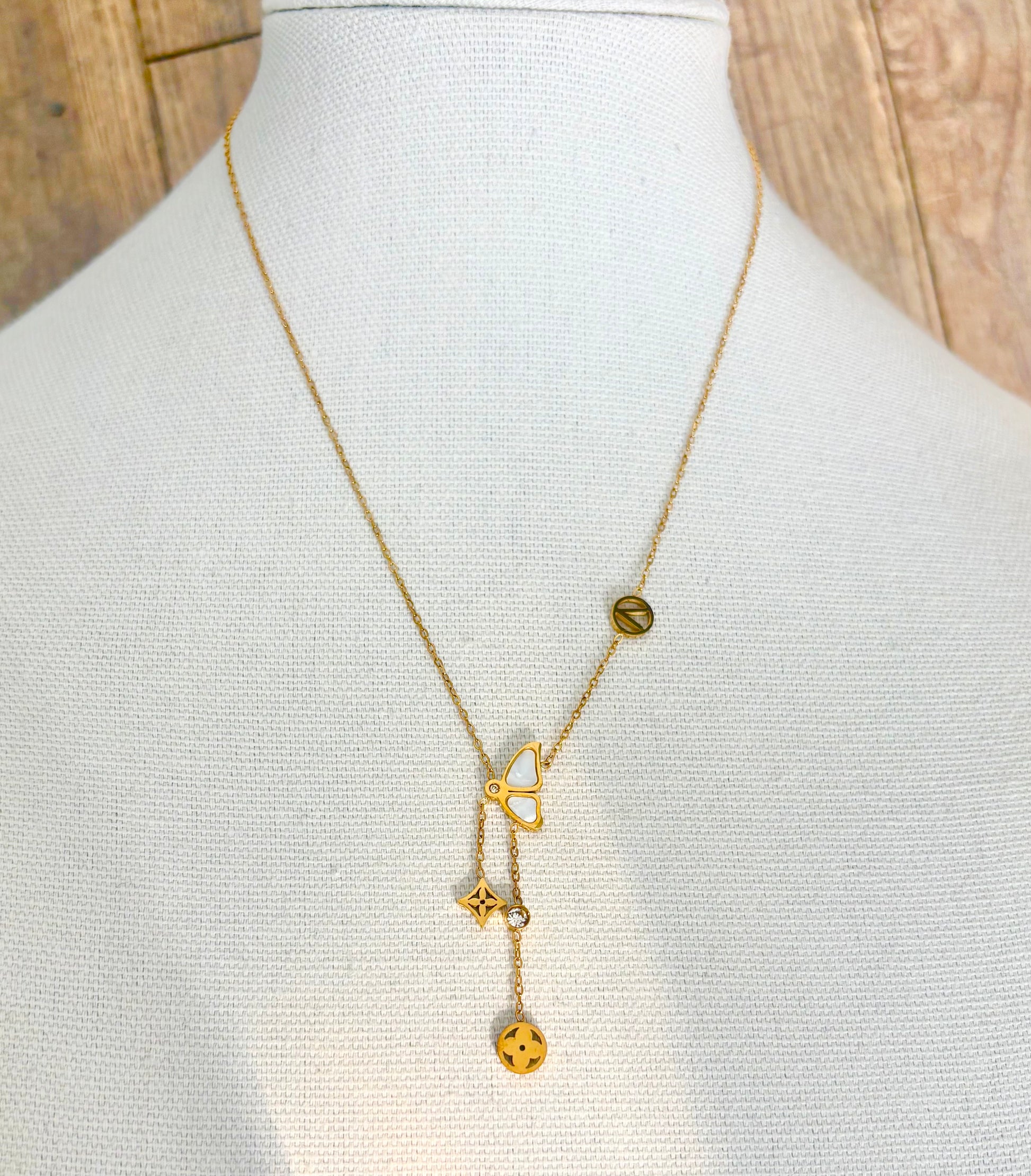A delicate gold Y-necklace a central butterfly charm with dangling clover and flower motifs, alongside a small round charm.