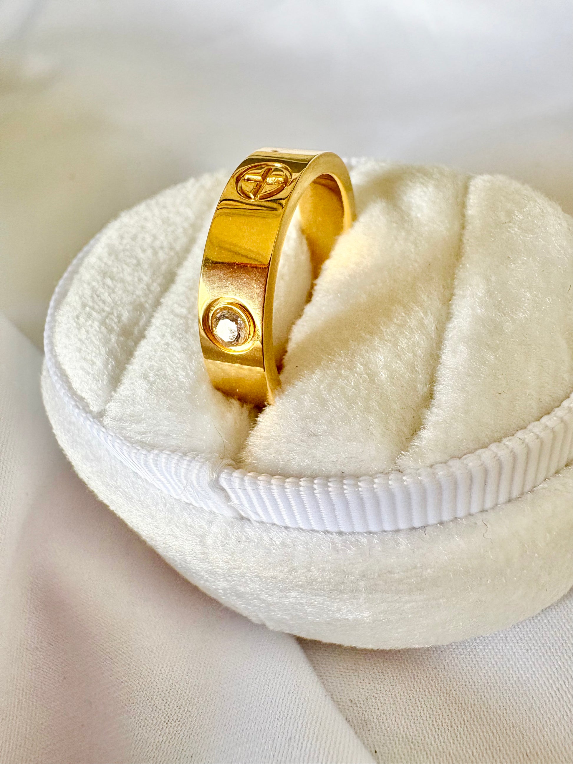 A gold band ring with a double cross motif and a small clear stone