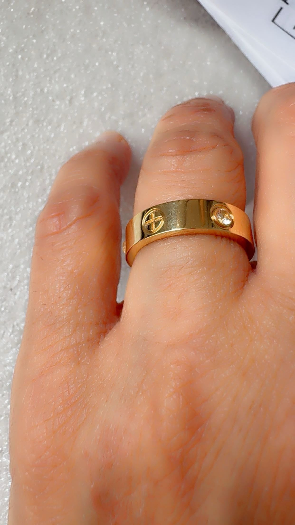 A gold ring with a screw-hole design and a small clear gemstone.