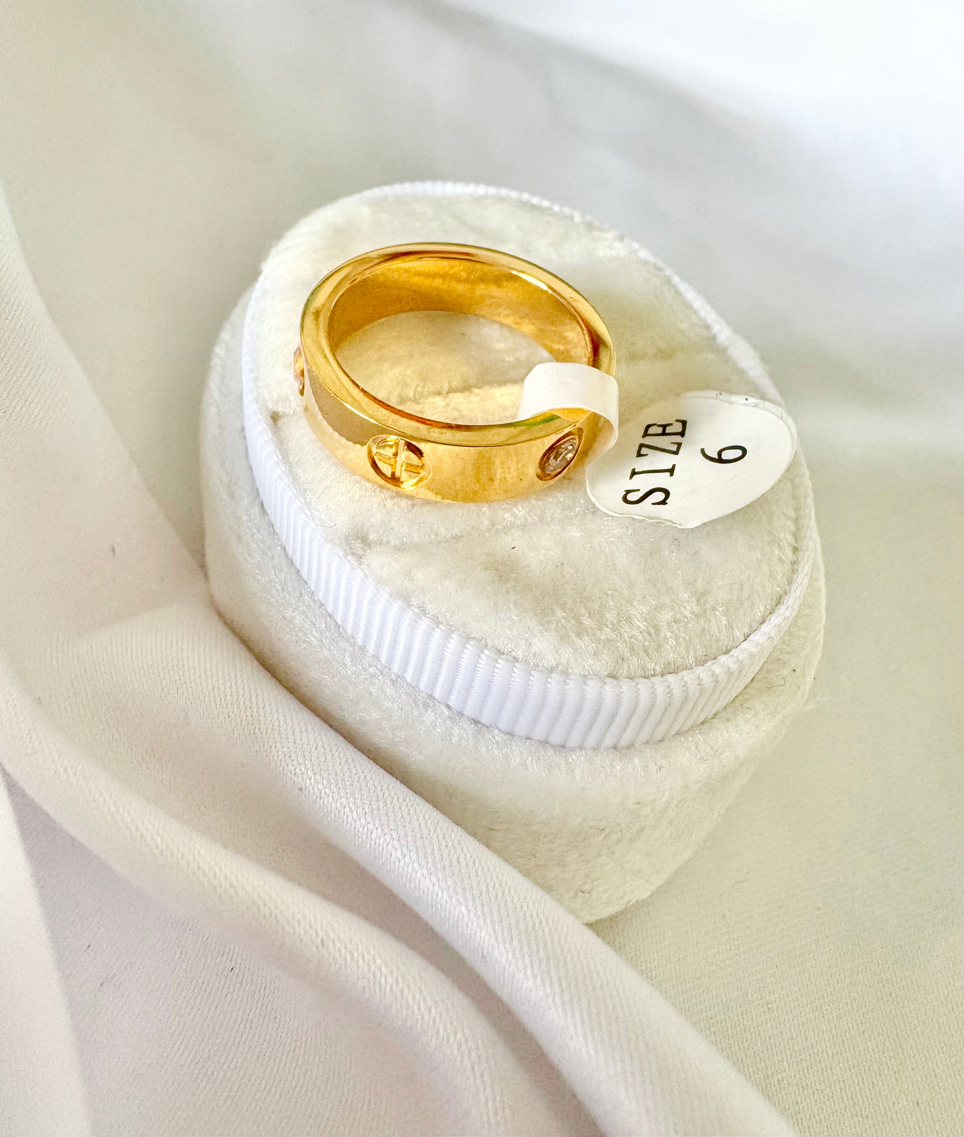 A gold ring displayed on a small white ring box with a small white tag reading SIZE 6
