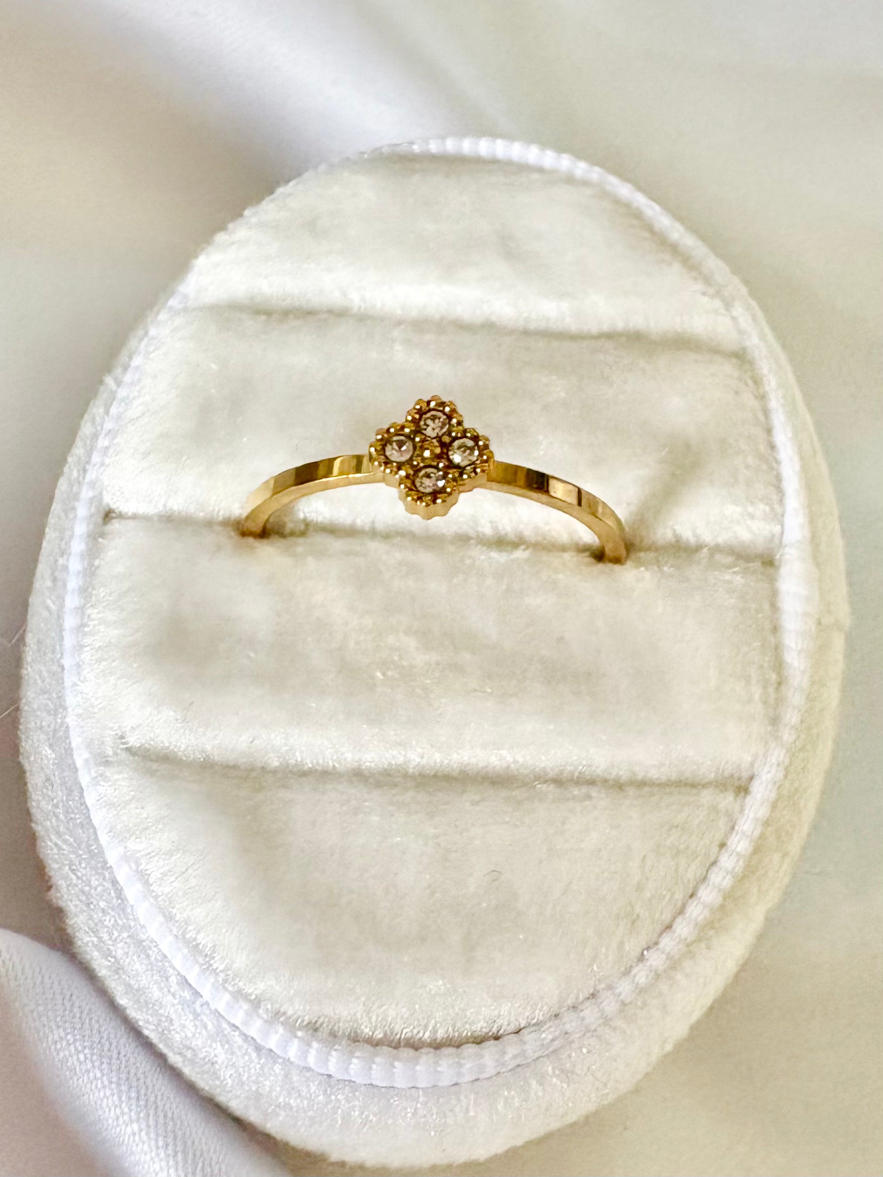 A gold ring with a small floral cluster of clear stones, displayed on a white velvet ring box.