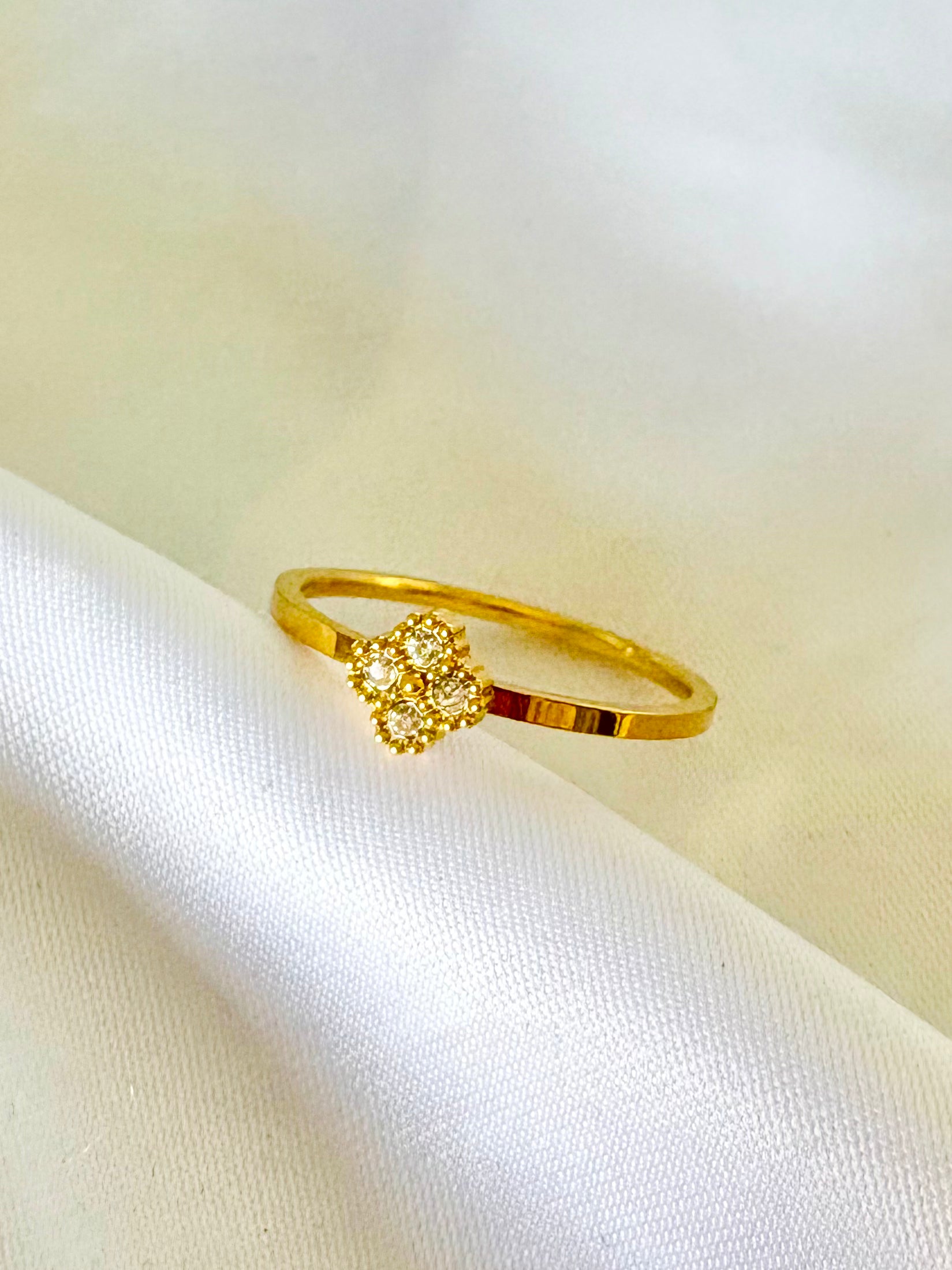 A gold ring with a small floral cluster setting, resting on draped white fabric.