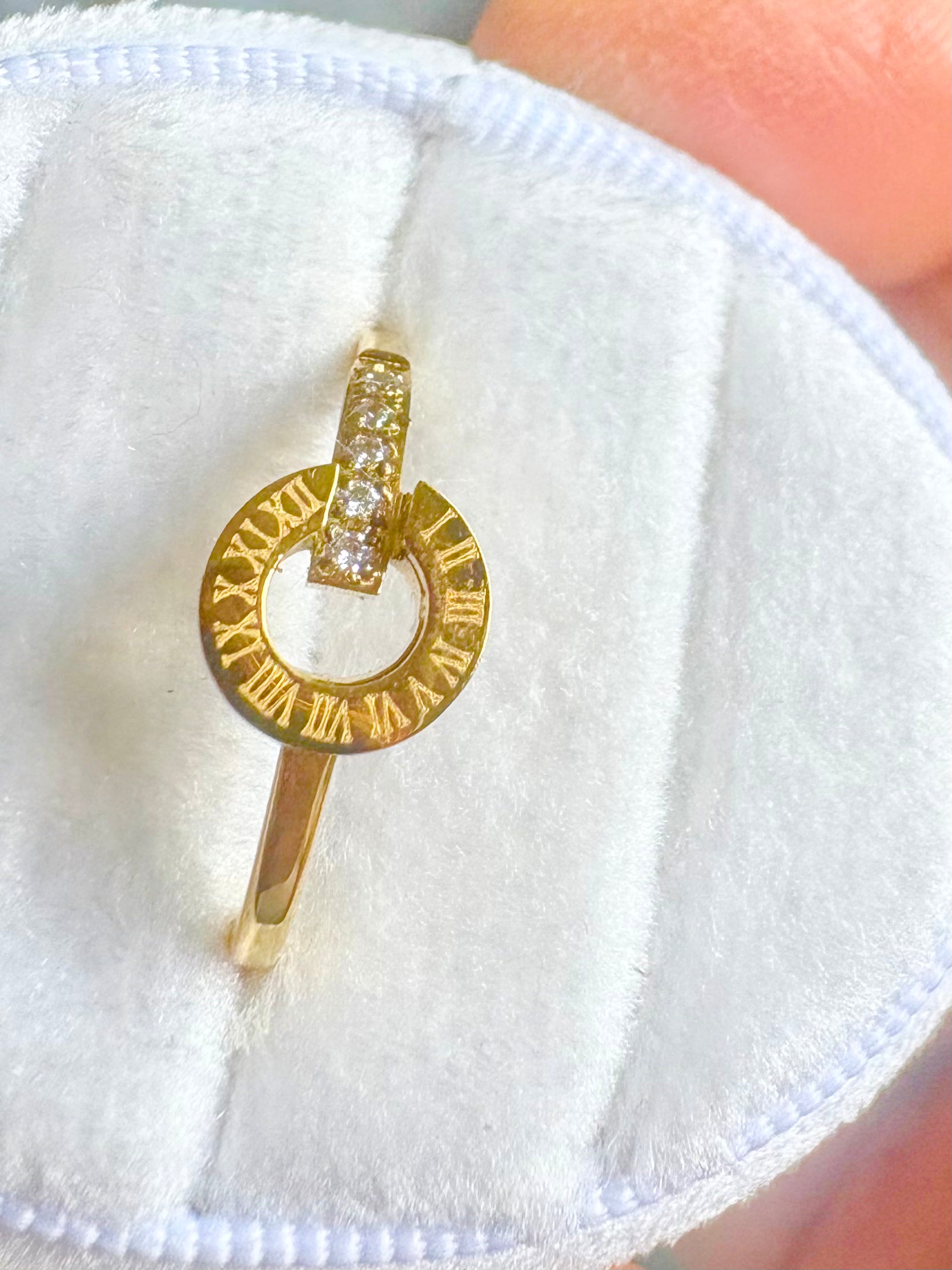 A gold ring with a circular Roman numeral design and a top bar set with small clear stones