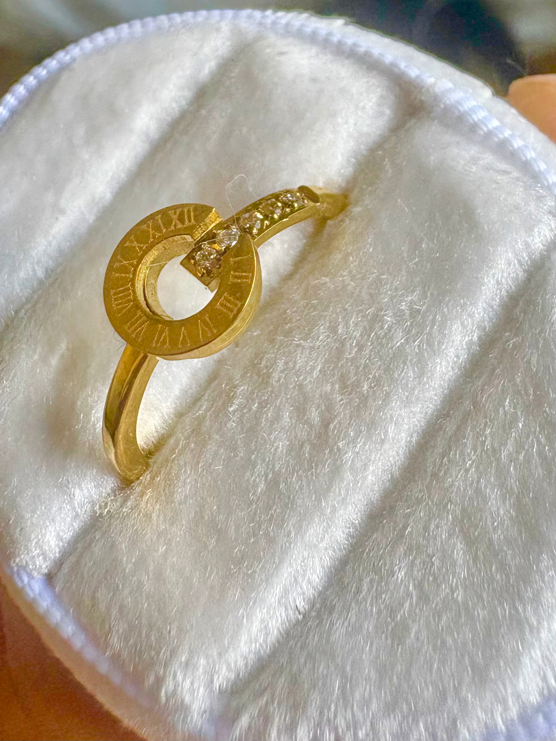 A gold ring with a circular Roman numeral design and a curved band set with small clear stones
