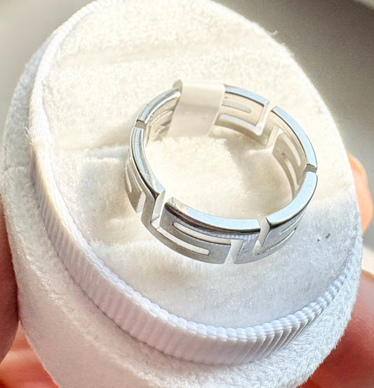 A silver geometric ring displayed on a white circular ring box