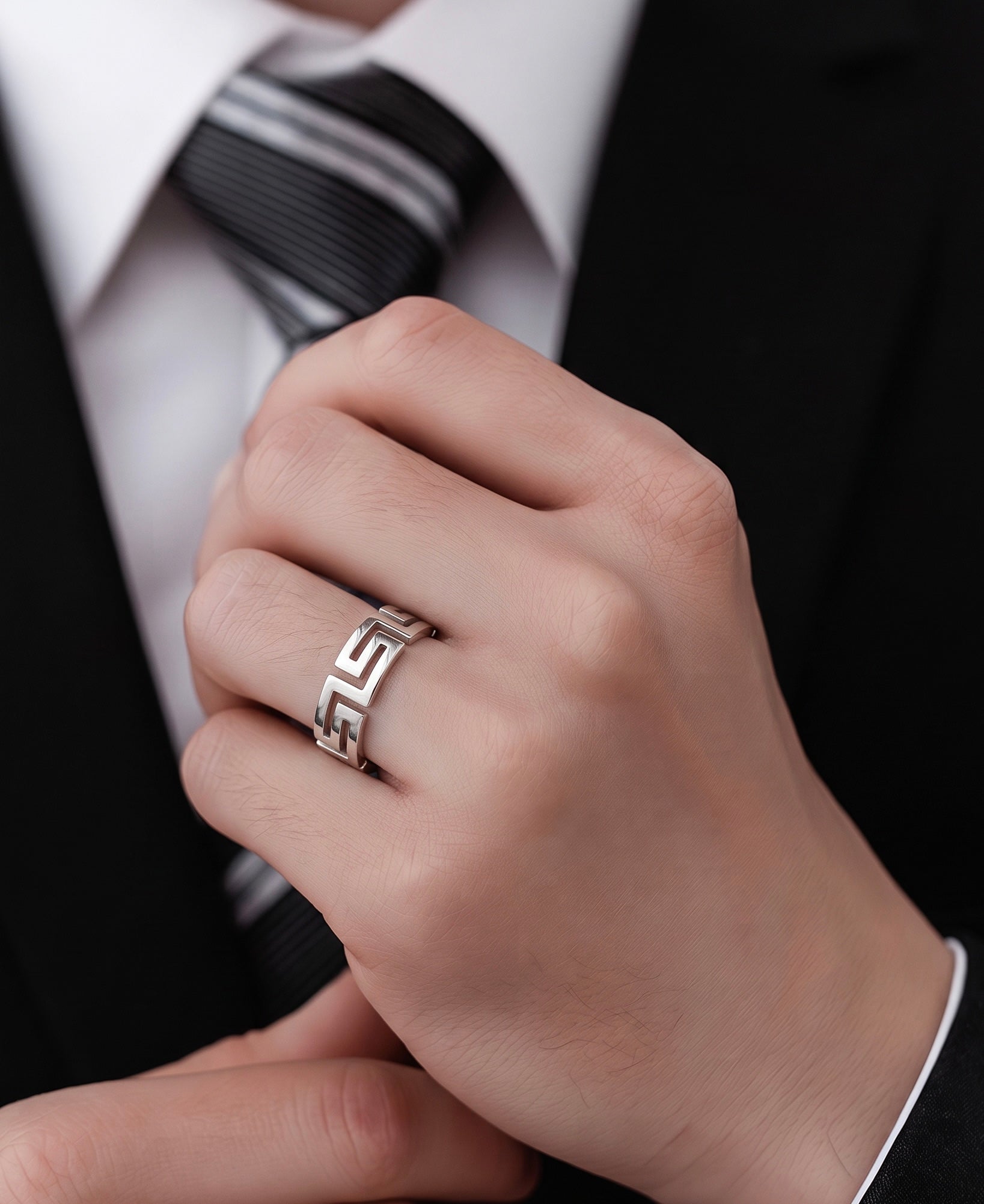 A close-up of a person's hand wearing a silver ring with a Greek key pattern