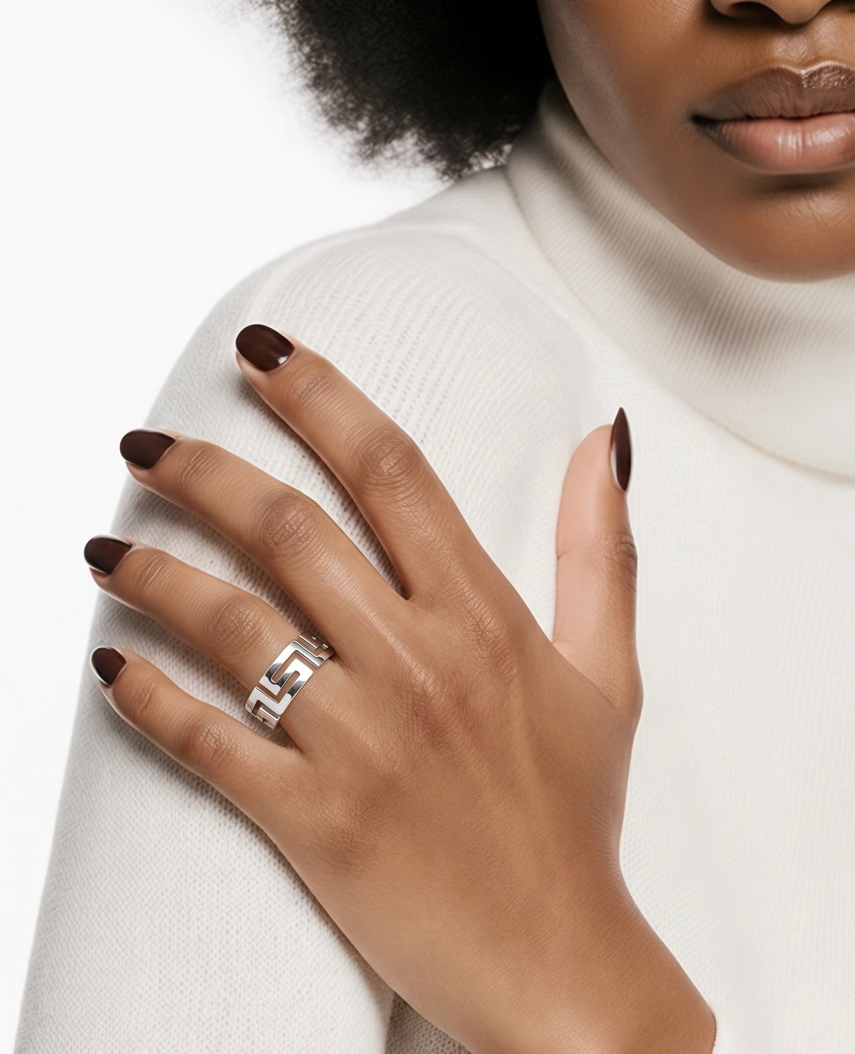 A close-up of a model's hand wearing a silver ring with a geometric interlocking pattern