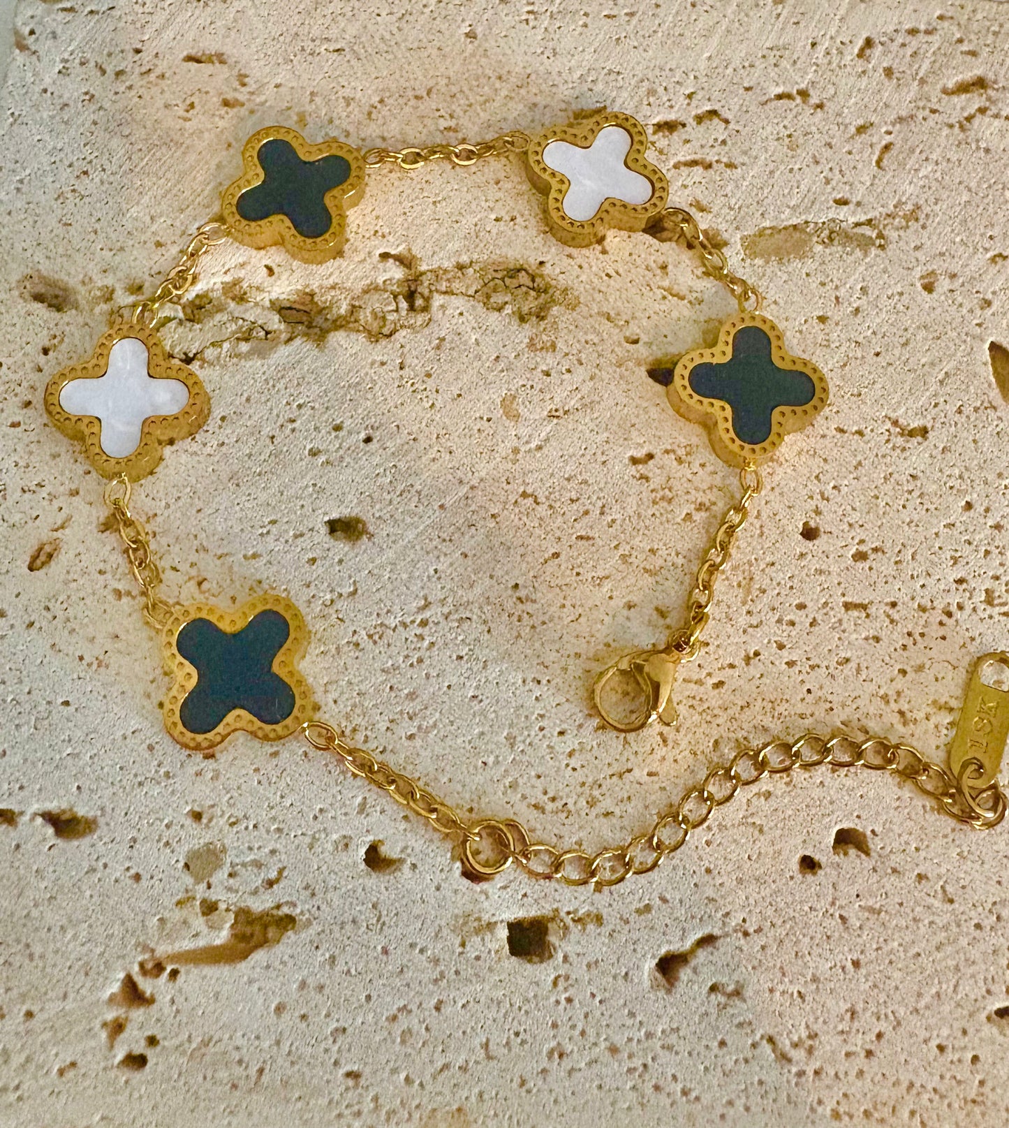 A gold-tone chain bracelet with five clover-shaped links, alternating between white and black .