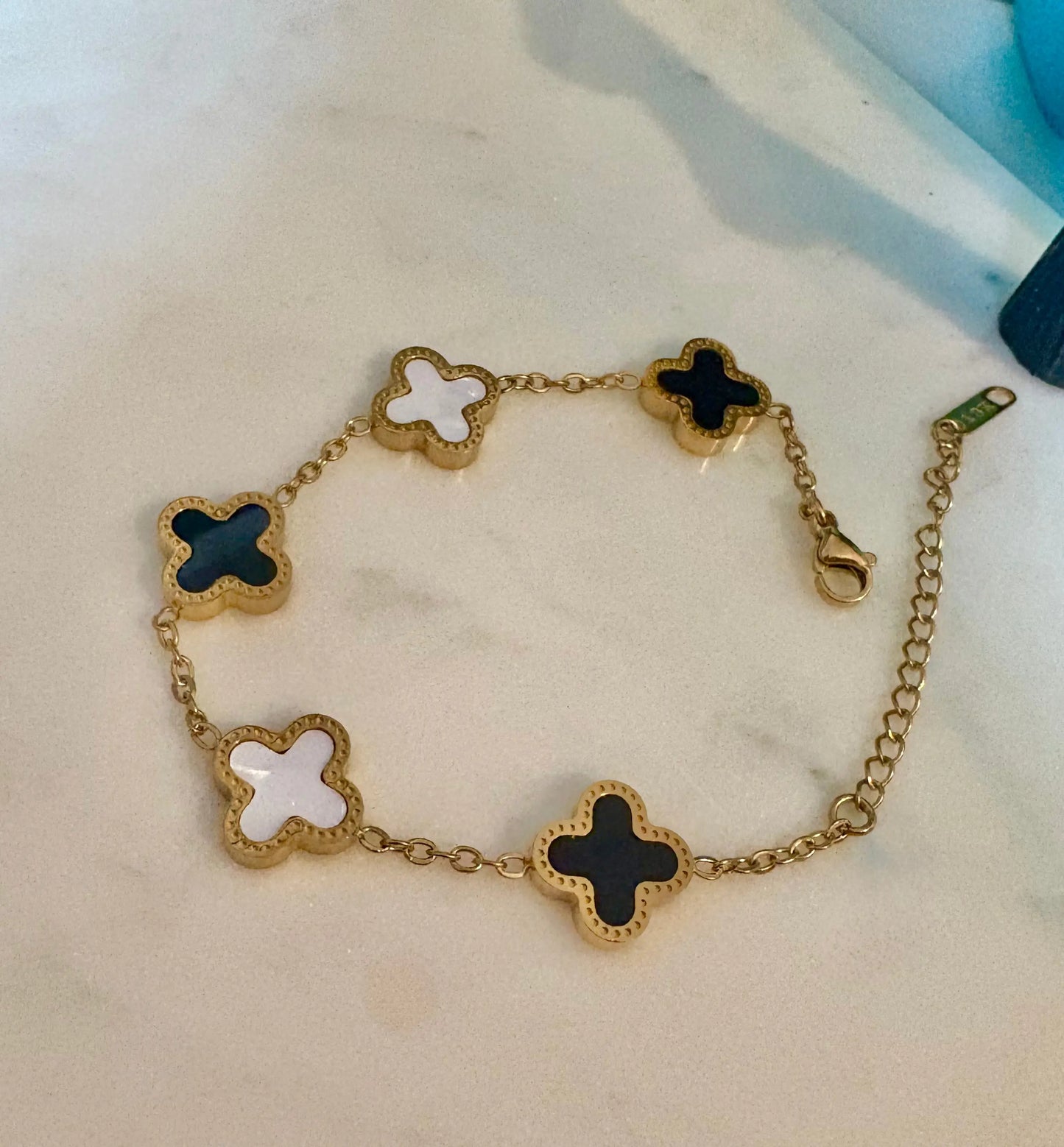 A gold-tone chain bracelet with five clover-shaped links, featuring alternating black and white enamel inlays