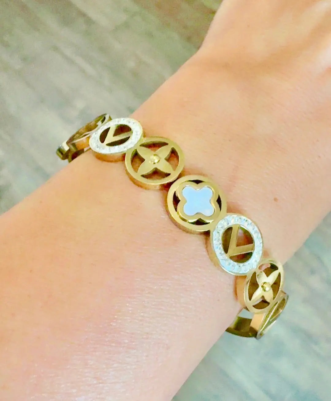 A gold-tone bracelet with circular links featuring star, clover, and chevron motifs, worn on a wrist.