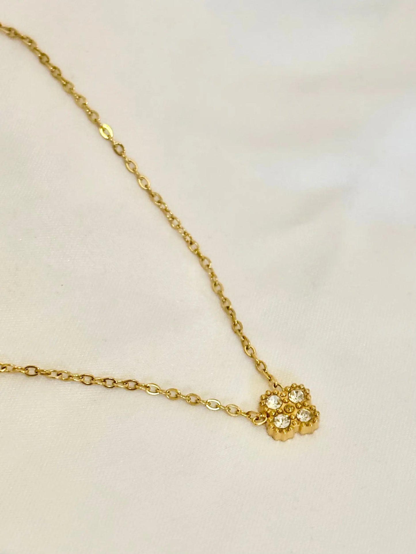 A delicate gold chain necklace featuring a small gold clover pendant with zircon stones
