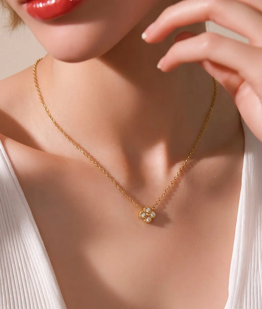 A close-up lifestyle shot of a model wearing a delicate gold chain necklace with a small clover pendant