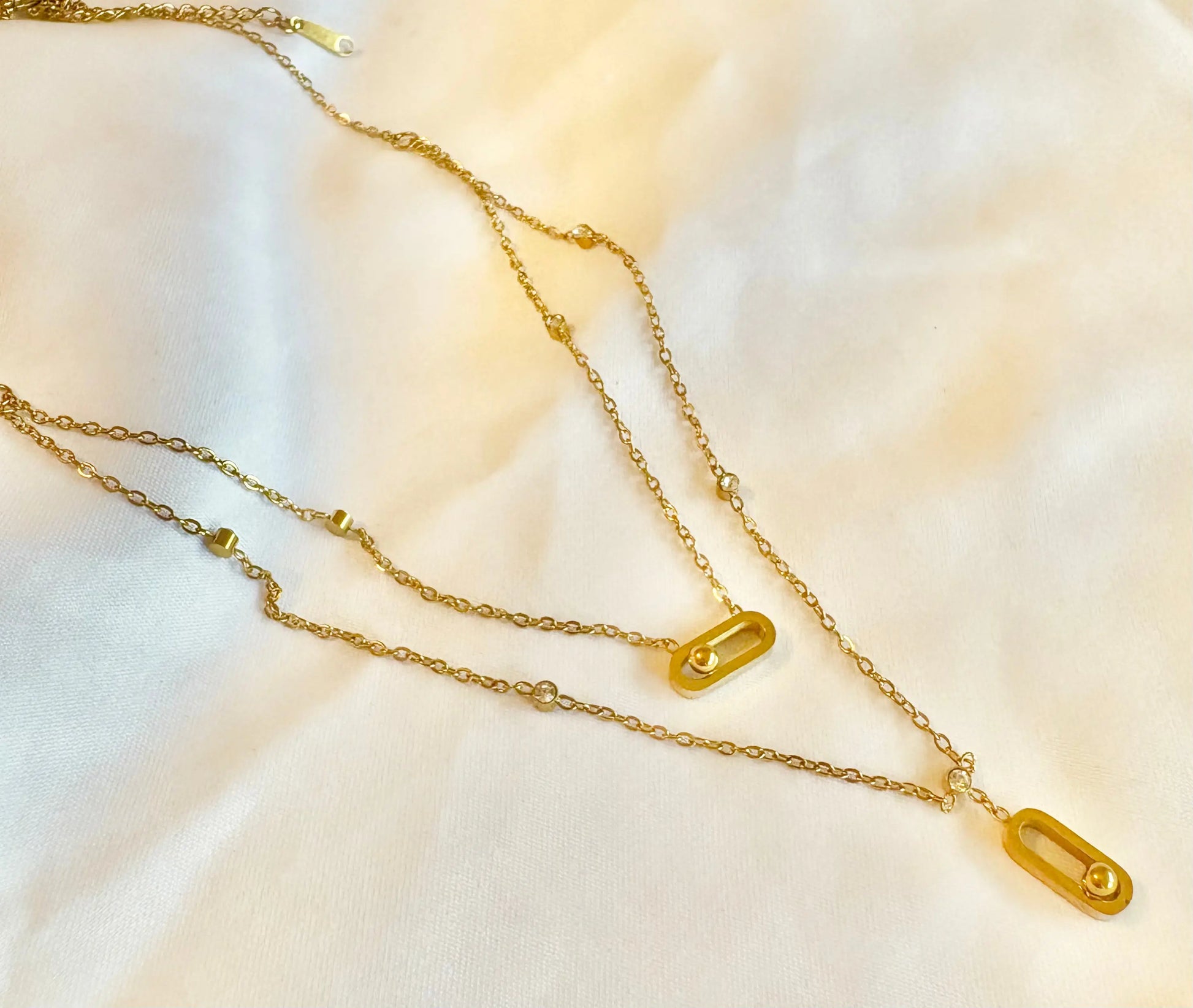 A gold chain necklace with two elongated capsule-shaped pendants