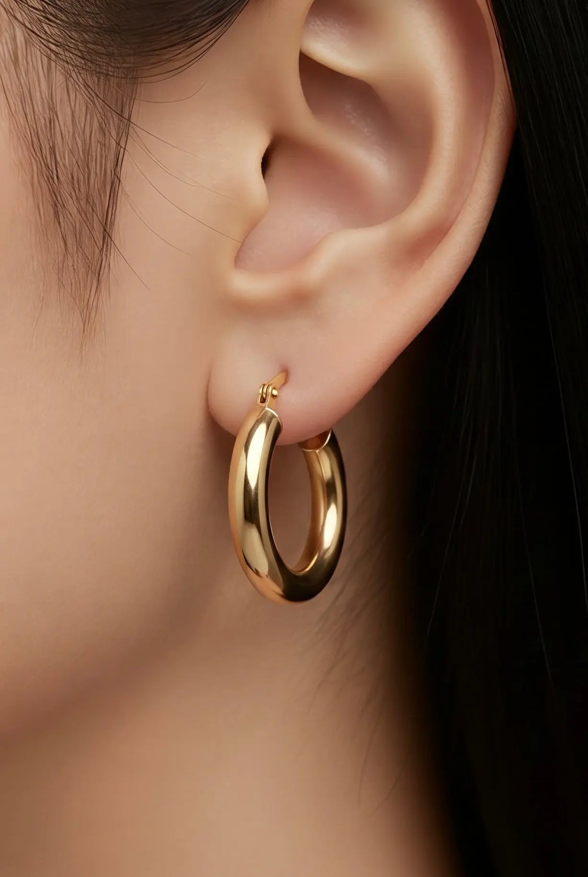 A close-up of a model's ear wearing a  gold plated hoop earring.