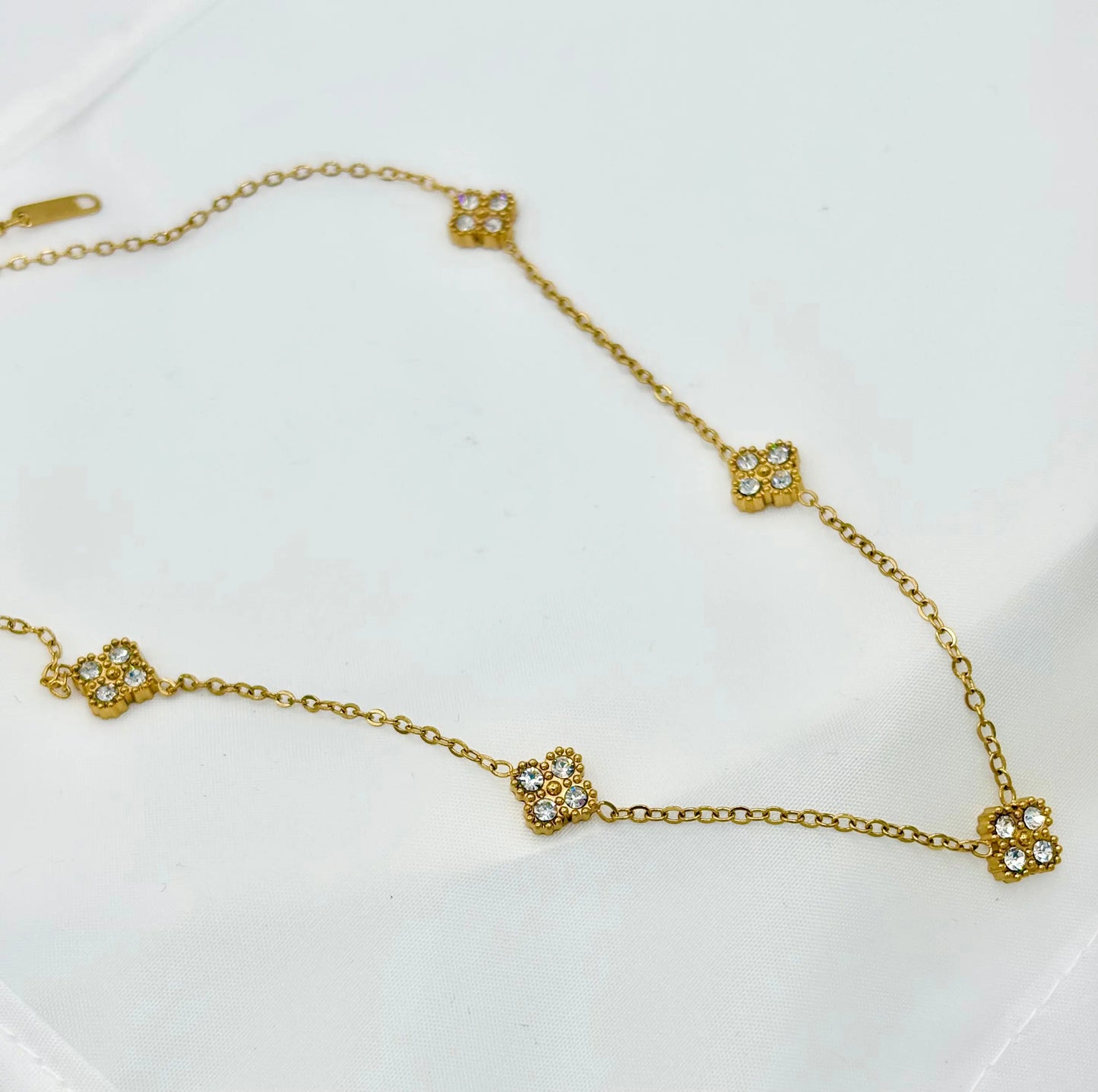 A delicate gold chain necklace featuring five small, clover-shaped of zircon pavé stones