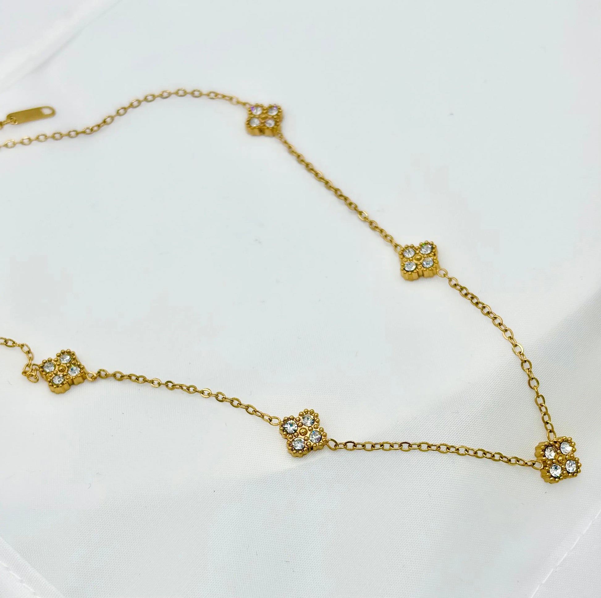 A delicate gold chain necklace featuring five small, clover-shaped of zircon pavé stones