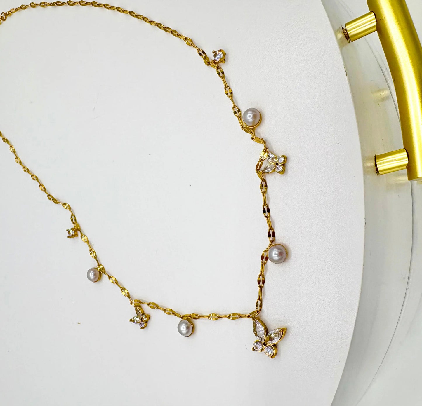 A delicate gold chain necklace featuring small clear rhinestone butterflies and several white freshwater pearls spaced along the chain