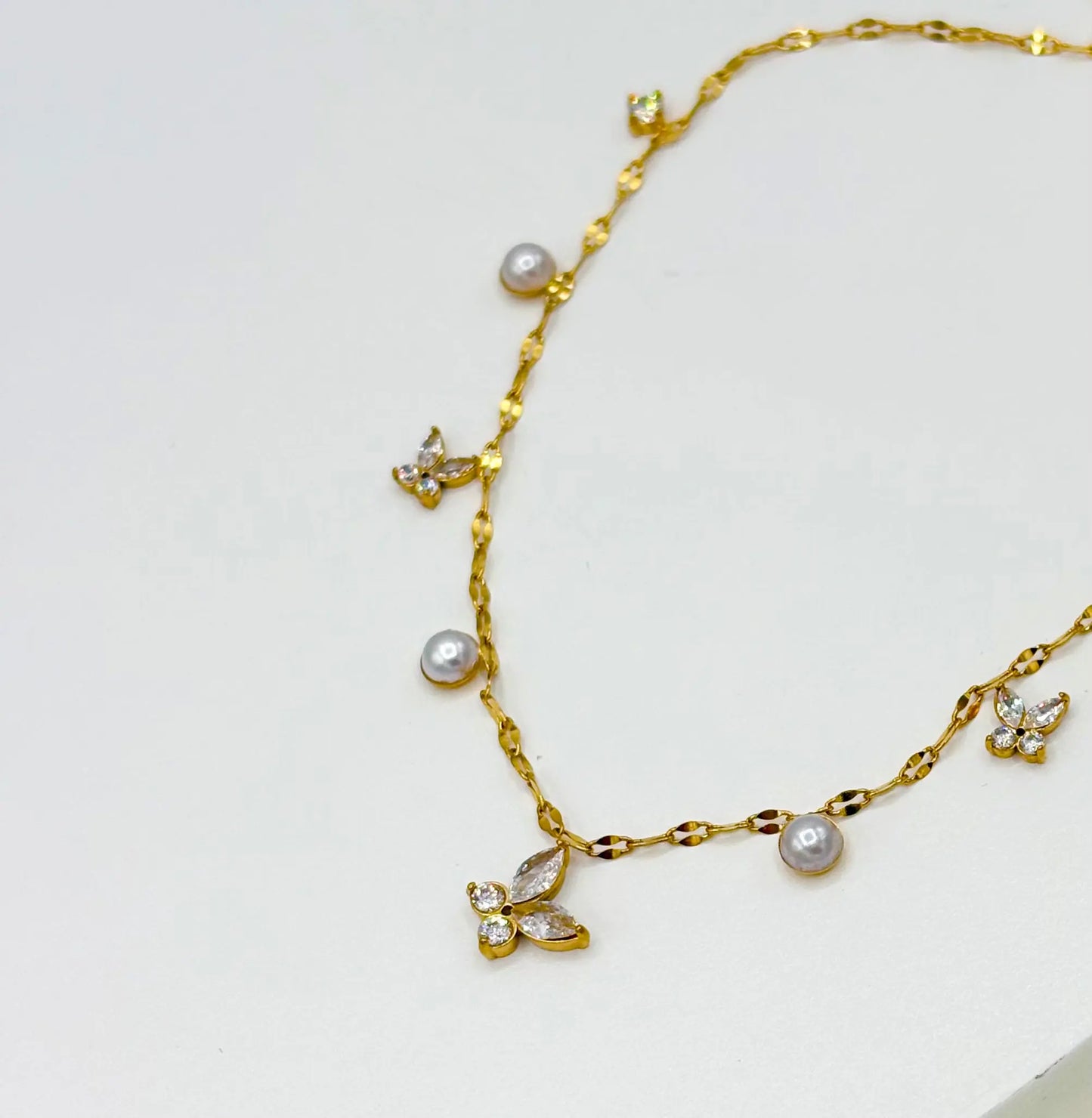 A delicate gold chain necklace featuring small butterfly and pearl charms