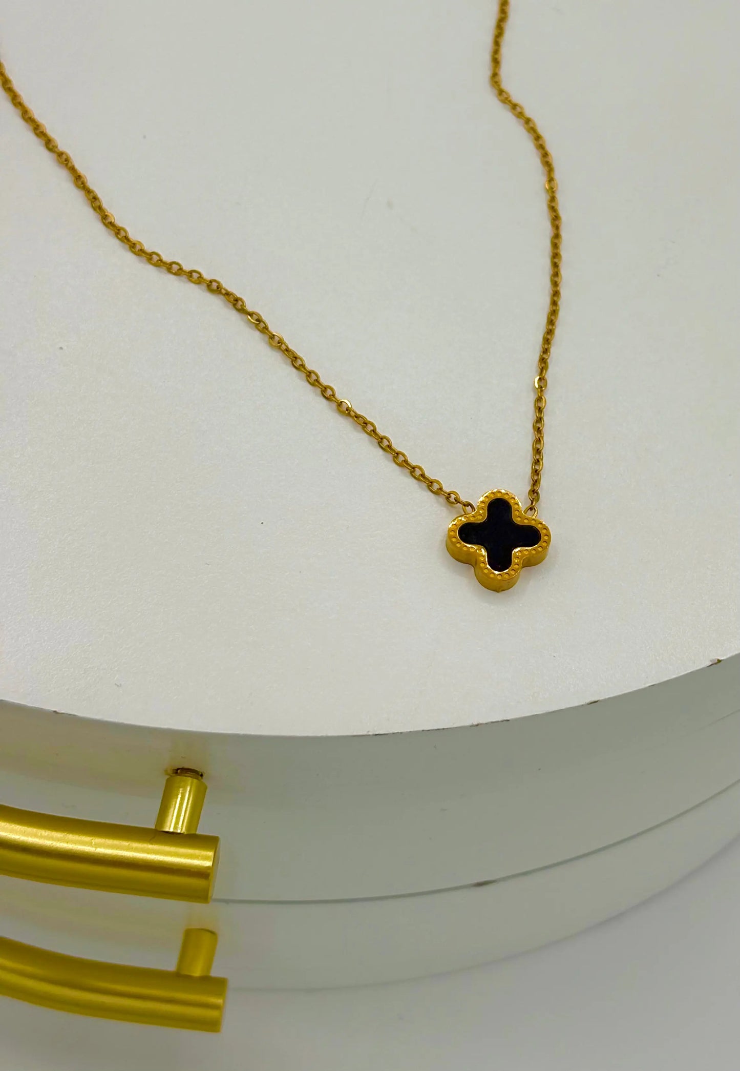 A gold chain necklace with a black clover-shaped pendant