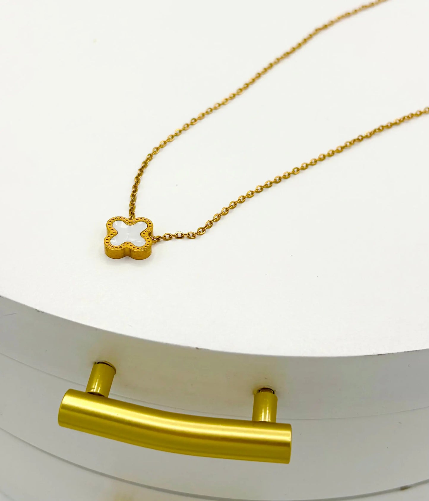A gold chain necklace with a small white clover-shaped pendant