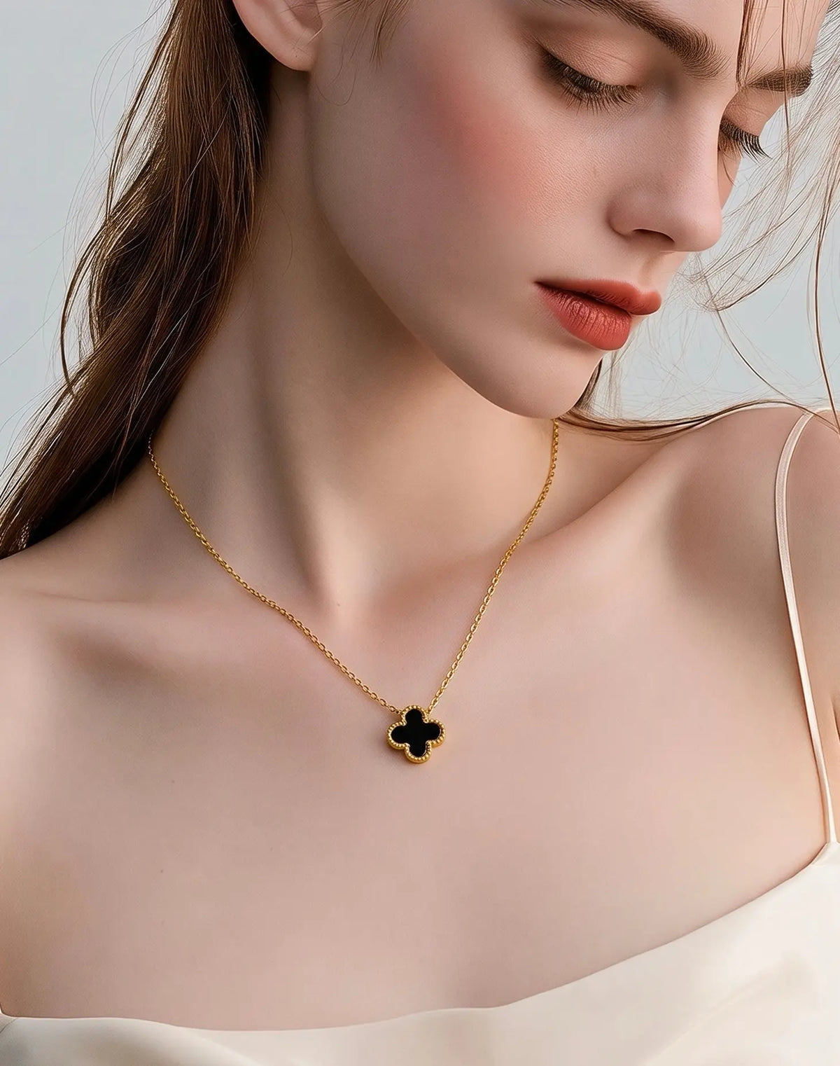 A close-up of a woman wearing a delicate gold chain necklace with a black clover pendant
